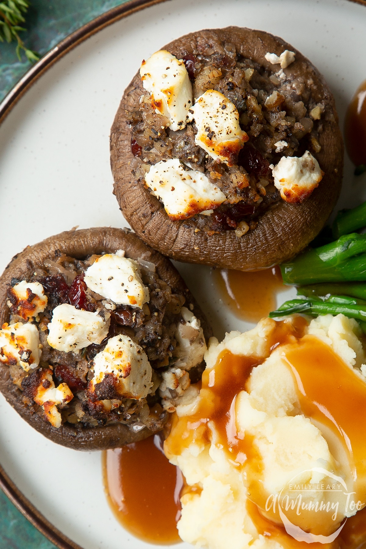 Overhead shot of crispy stuffed mushrooms topped with goats cheese and mashed potato on the side served on a white plate with a mummy too logo in the lower-right corner