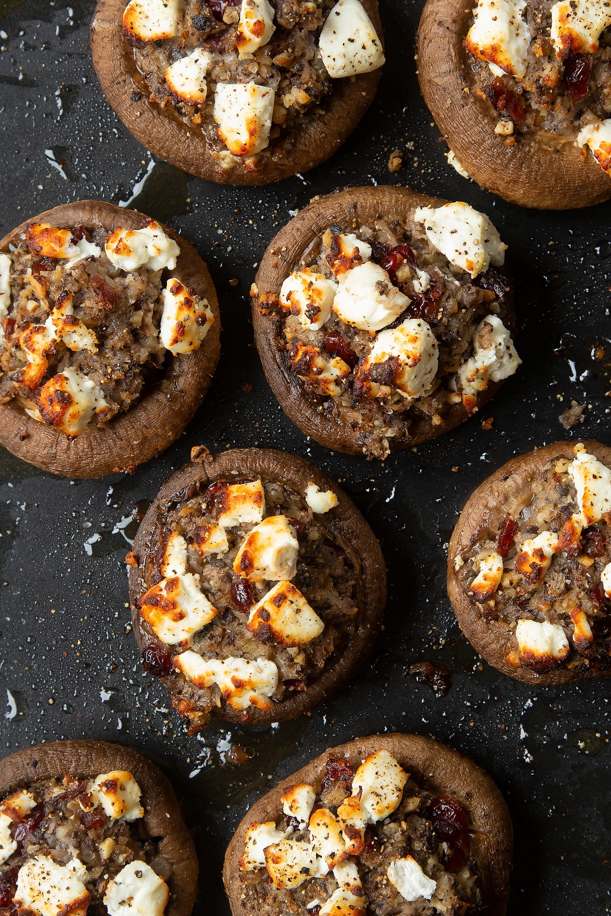 Overhead shot of crispy stuffed mushrooms topped with goats cheese on a baking tray