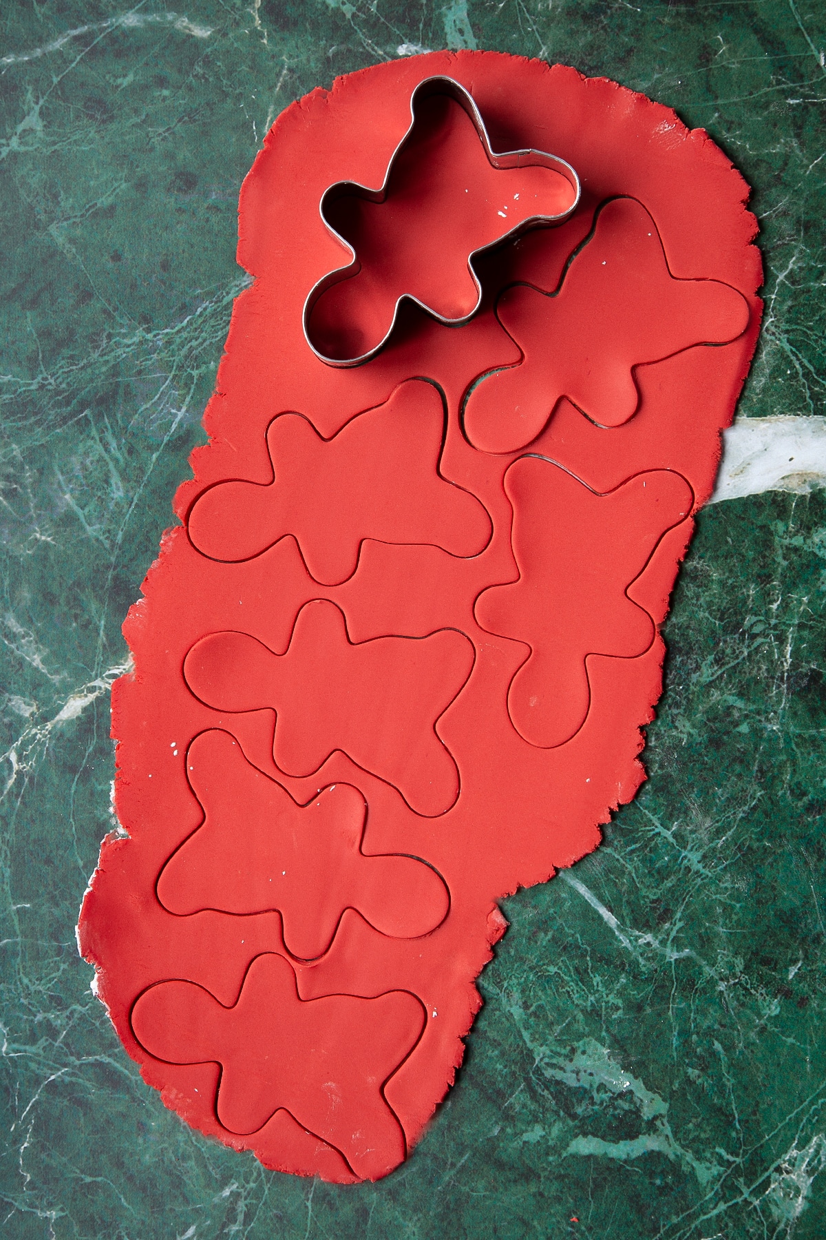 Red sugar paste rolled out on a green marble surface. A gingerbread man cutter has cut several shapes.