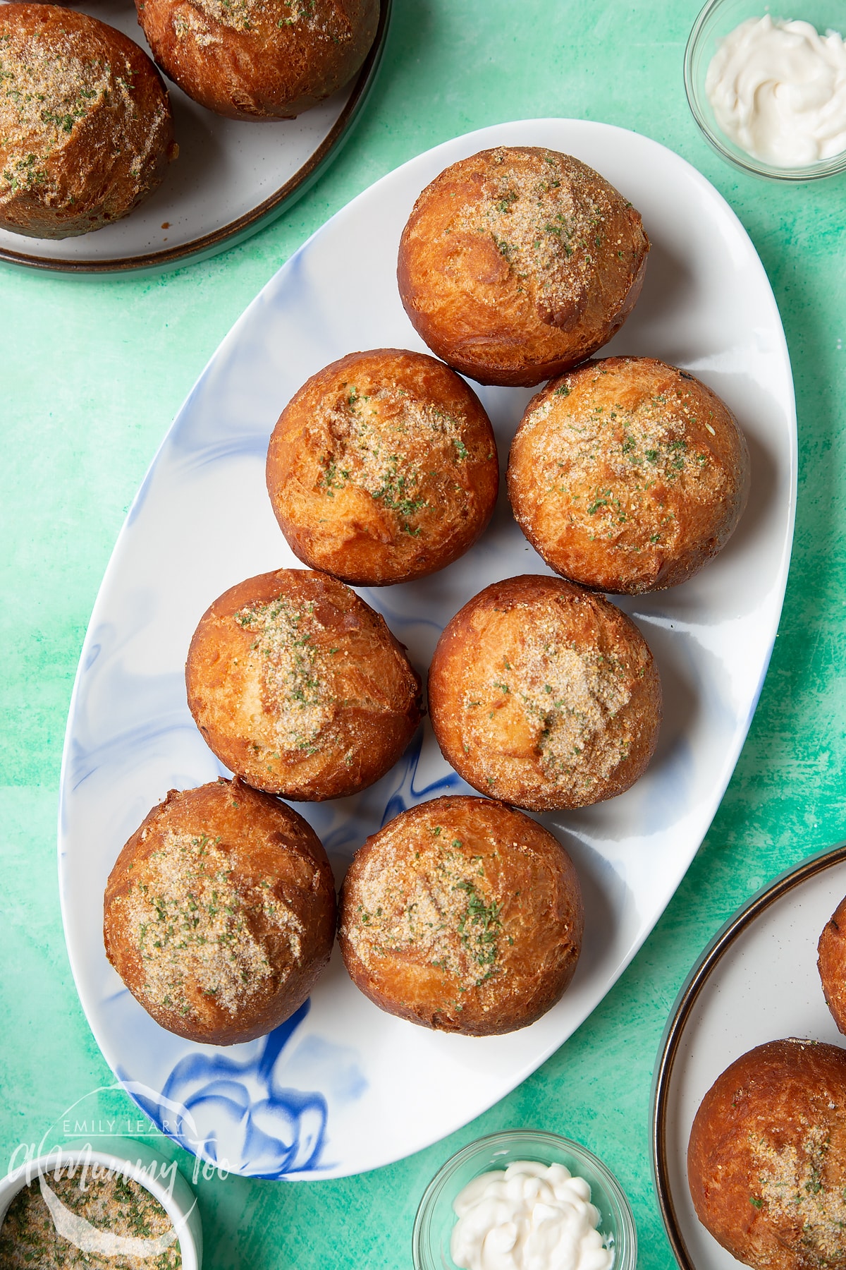 Pulled chicken doughnuts, sprinkled with savoury dust on an oval plate surrounded by condiments.