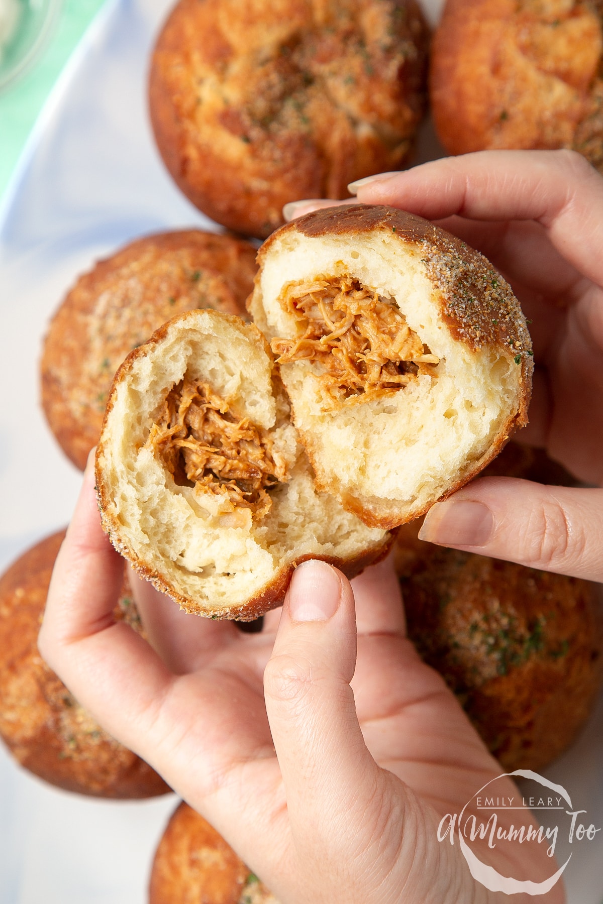 Two hands holding a pulled chicken doughnut broken open.