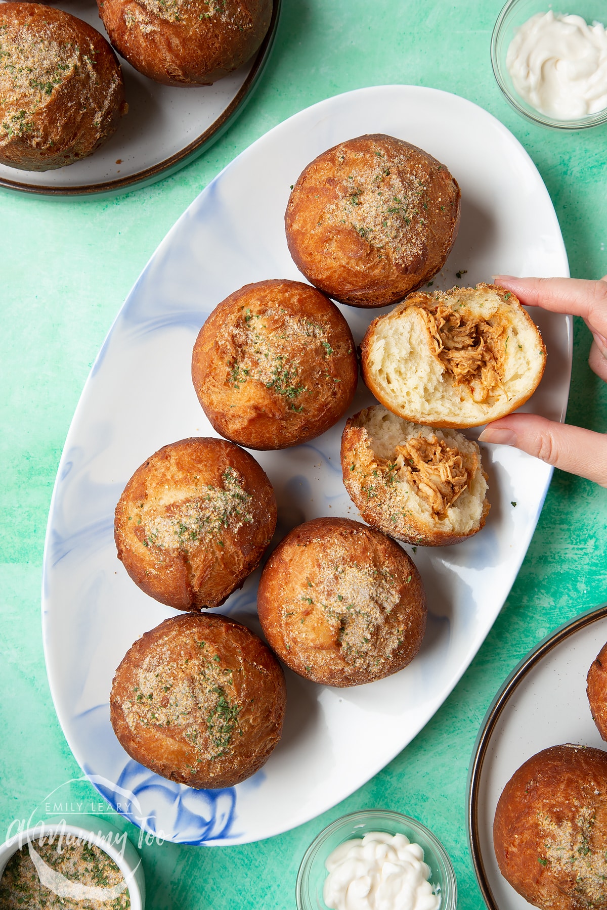 Pulled chicken doughnuts on an oval plate. One is broken open. A hand reaches to take it.