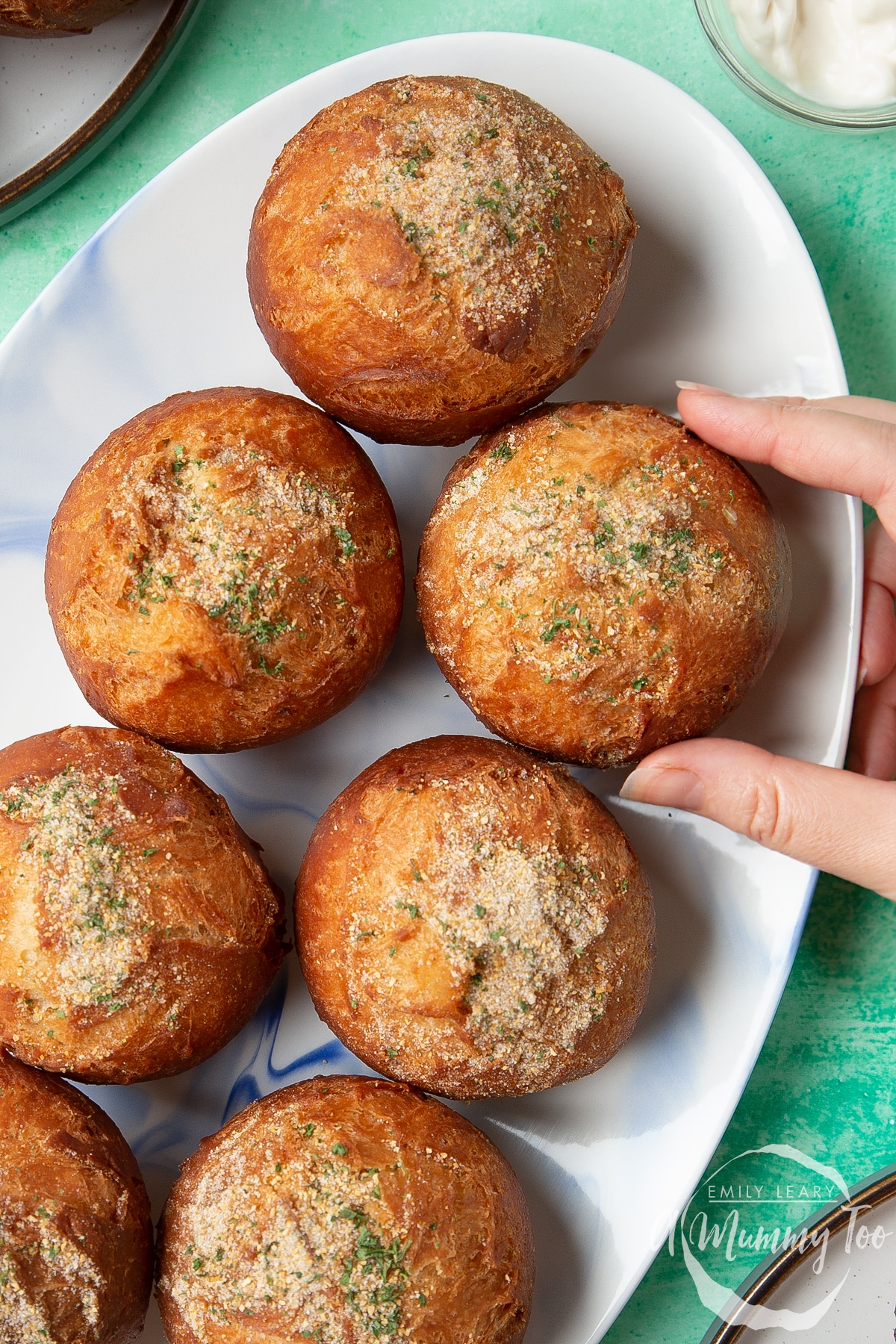 Pulled chicken doughnuts on an oval plate. One is broken open. A hand reaches to take one.