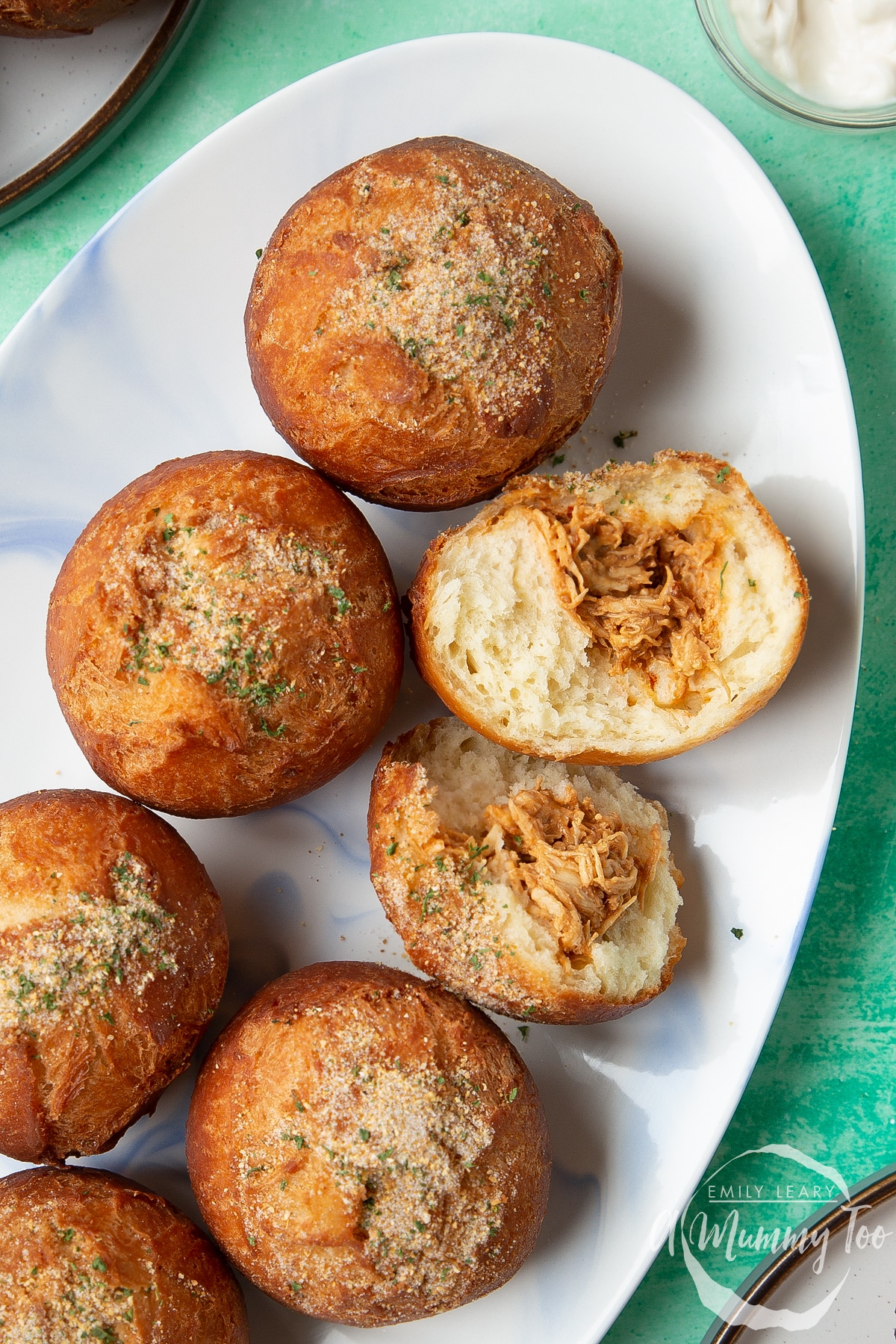 Pulled chicken doughnuts, sprinkled with savoury dust on an oval plate. One doughnut is torn open.