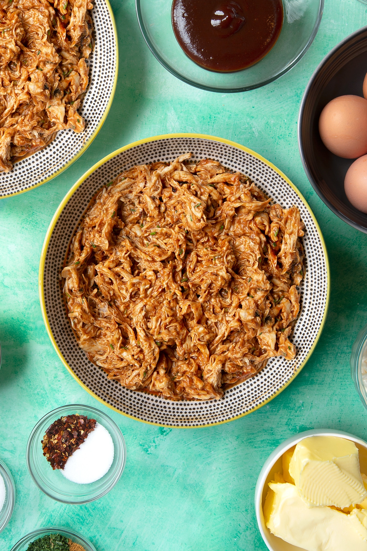Pulled barbecue chicken breast in a bowl. Ingredients to make chicken doughnuts surround the bowl.