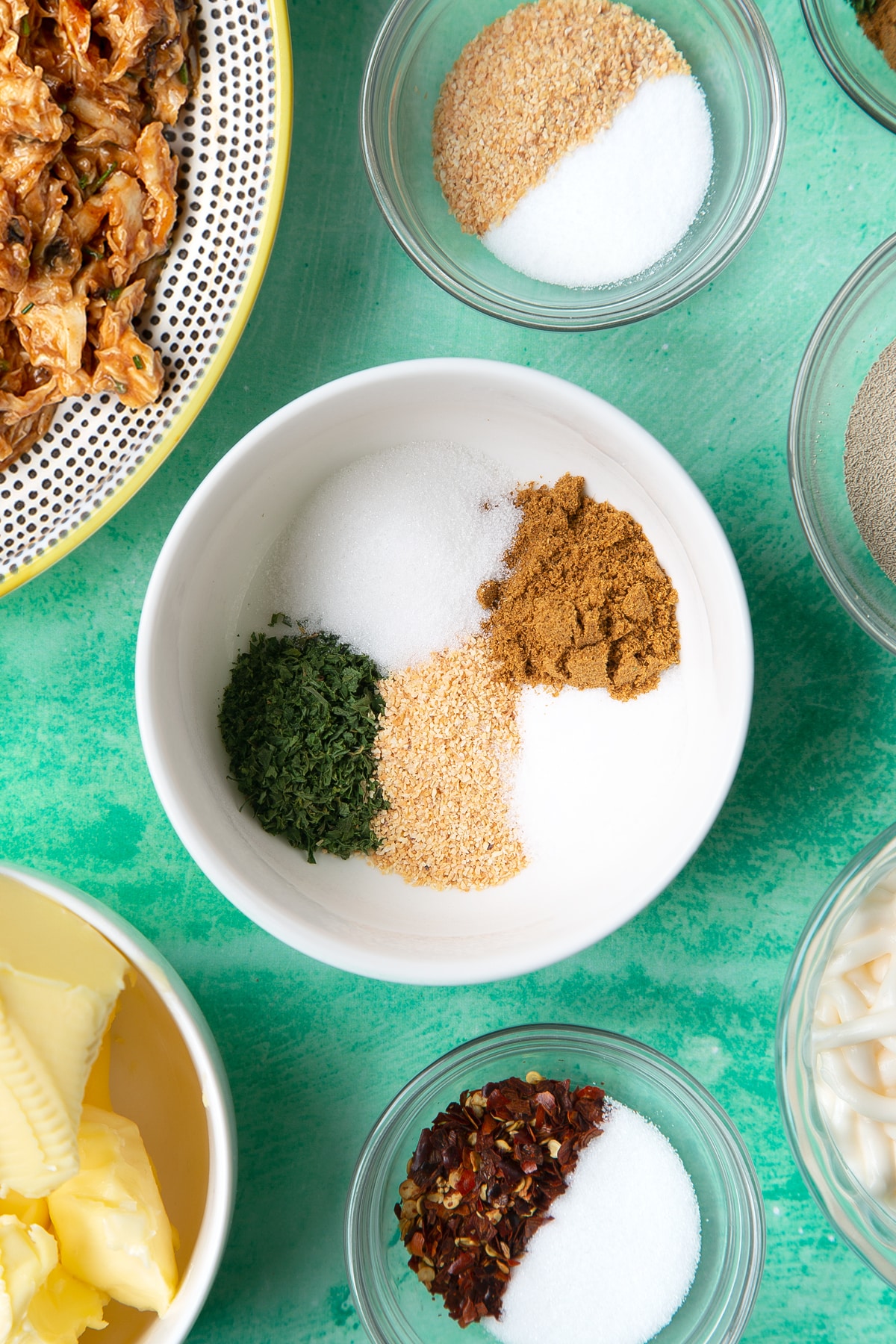 A small white bowl containing cumin, garlic granules, sugar, salt and dried coriander.