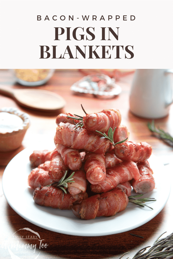 Forward facing shot of a stack of pigs in blankets on a white plate. In the background there's some of the tools needed to for the recipe.