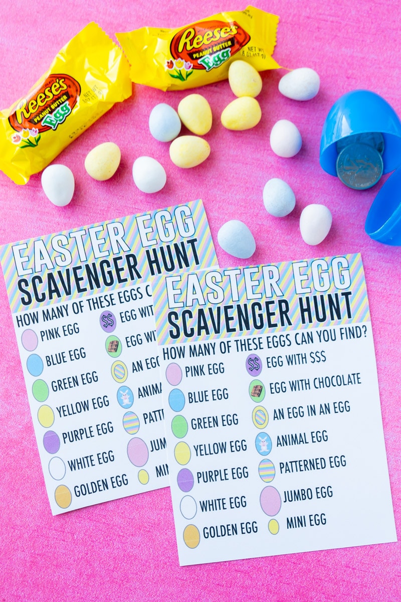 Two Easter Egg scavenger hunt cards on a pinch surface surrounded by chocolate eggs. The cards challenge hunters to find various eggs such as "blue egg", "patterned egg" etc.