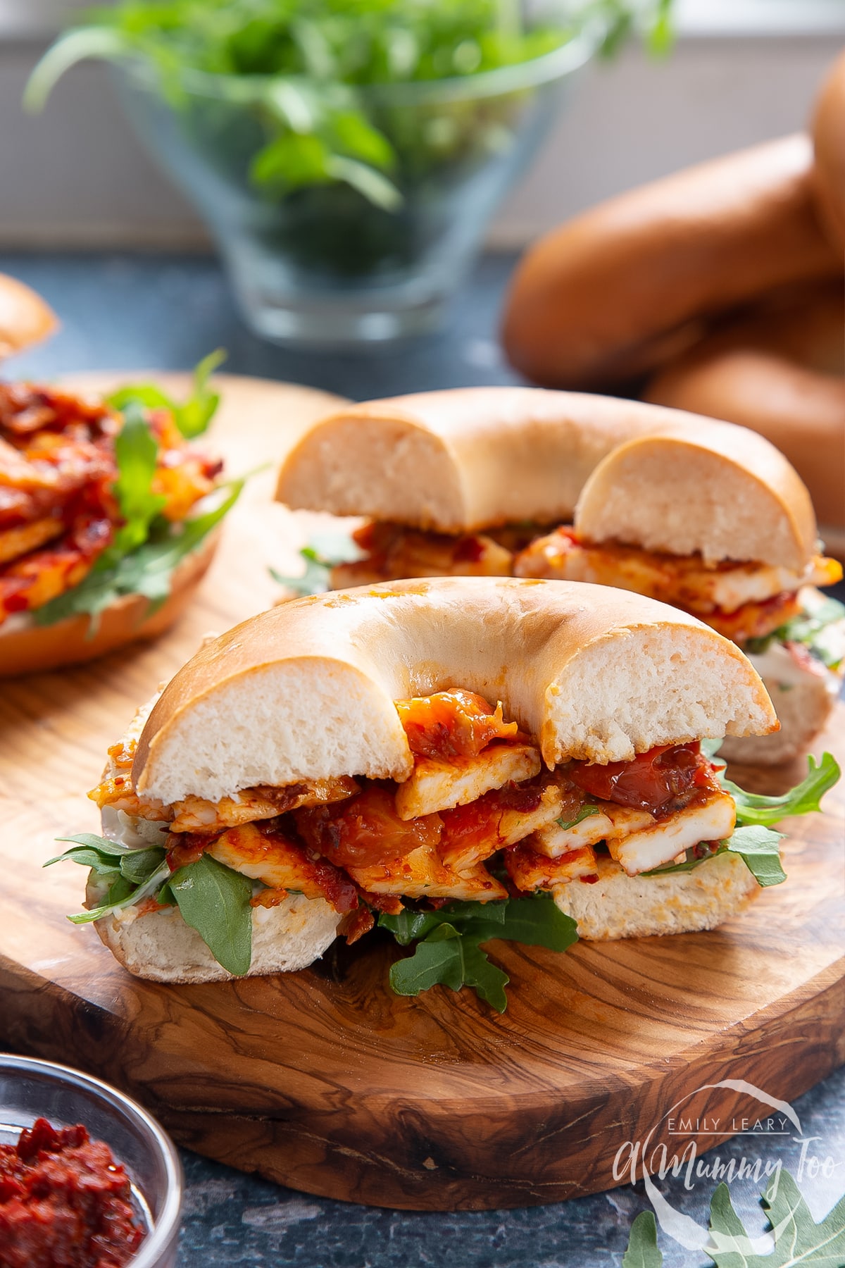 Two halloumi bagels on a wooden board. One is cut in half.