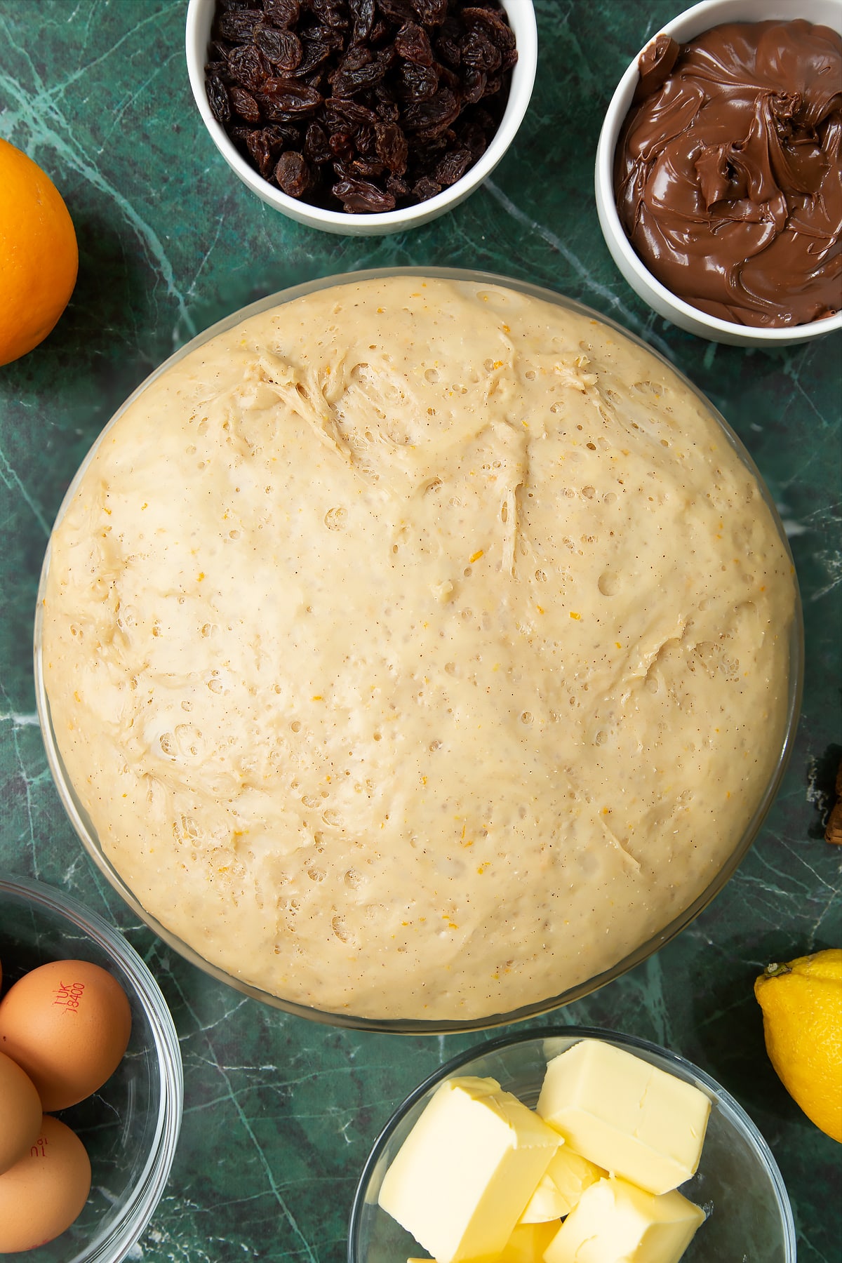 Proved spiced bread dough in a bowl. Ingredients to make Nutella panettone surround the bowl.