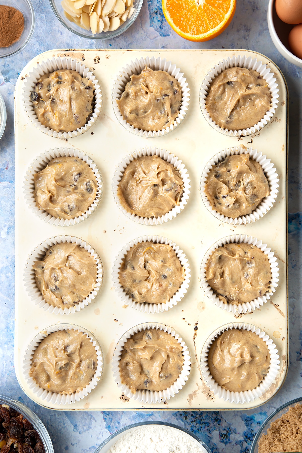 Overhead shot of orange and cinnamon muffin mix in muffin cases in a muffin tray