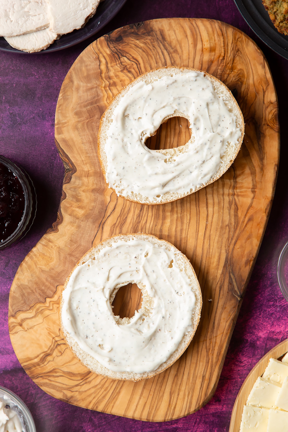 Overhead shot of halved turkey bagel with spread on a wooden plate
