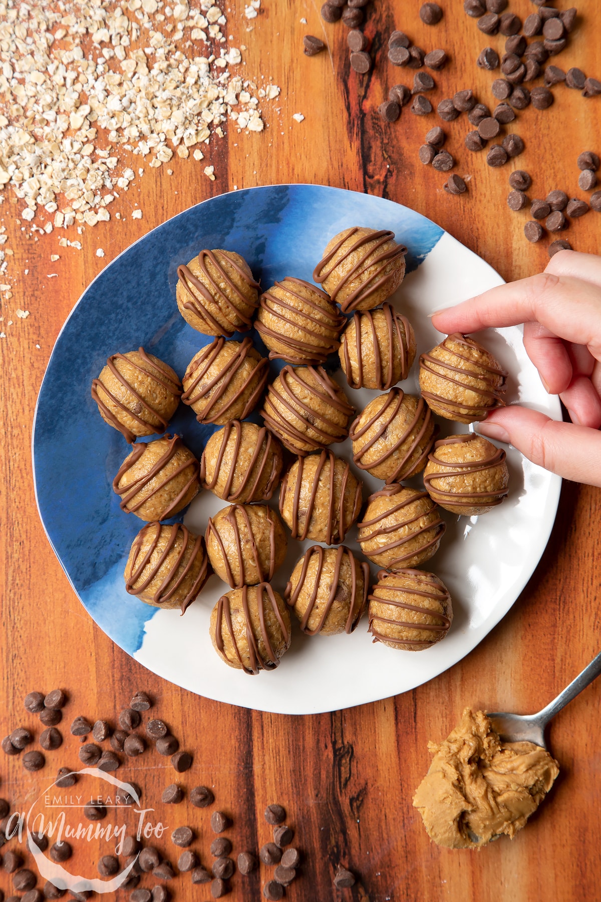 3 ingredient peanut butter and oatmeal balls decorated with chocolate on a blue and white plate. A hand reaches to take one.