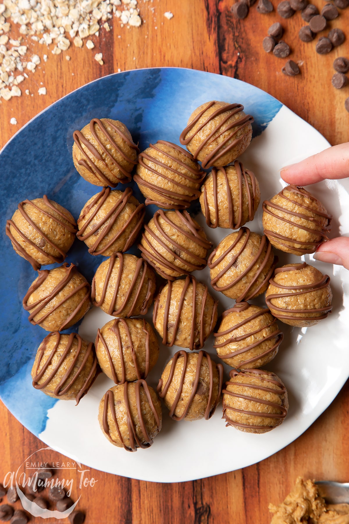 Peanut butter and oatmeal balls decorated with chocolate on a blue and white plate. A hand reaches for one.