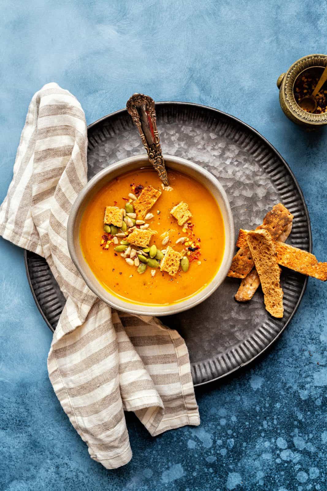 Three bowls of butternut squash soup on a dark blue table top. In the corner there's a black pan with more butternut squash soup.