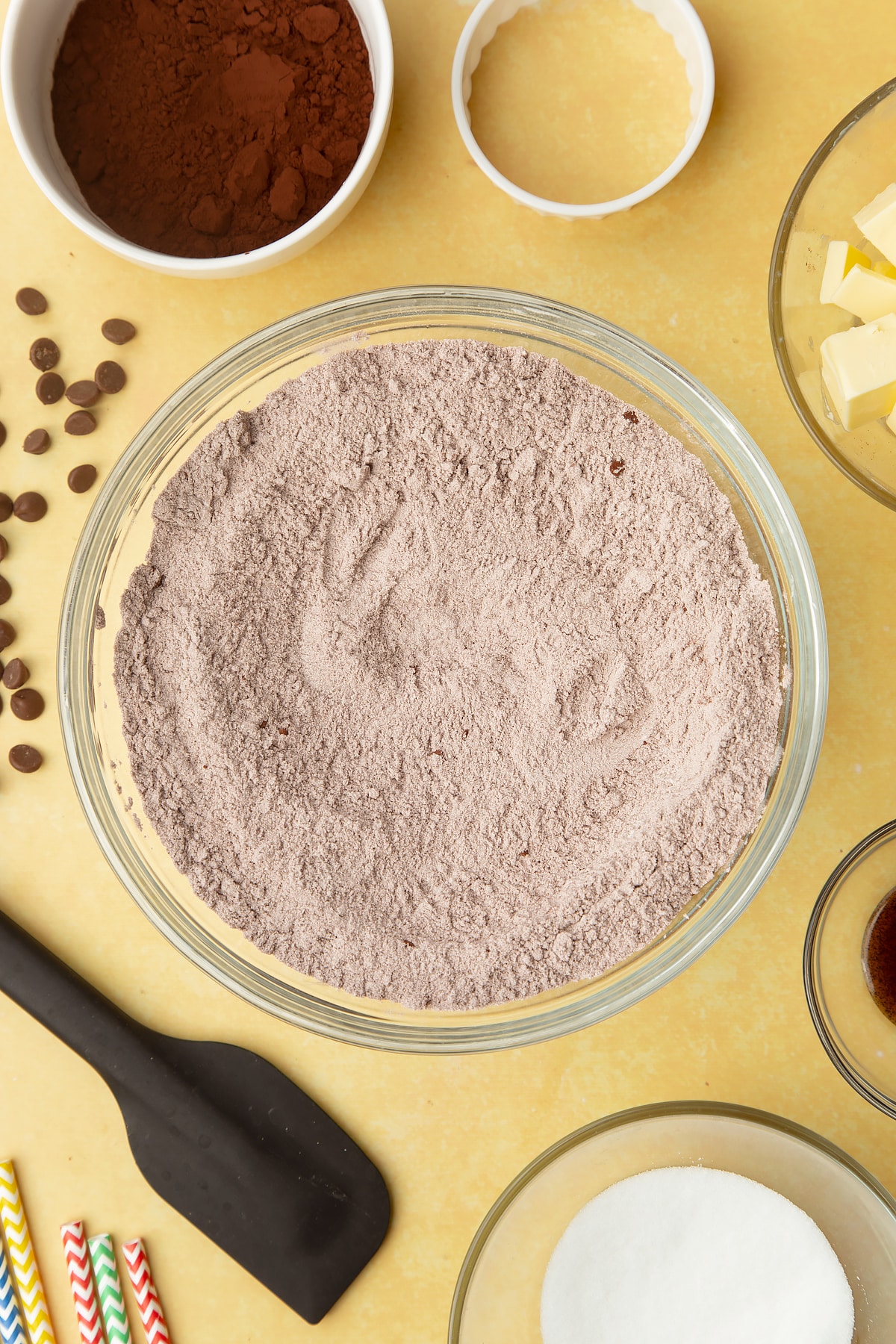 Cocoa, sugar, flour mixed together in a bowl. Ingredients to make Nutella sandwich cookies surround the bowl.