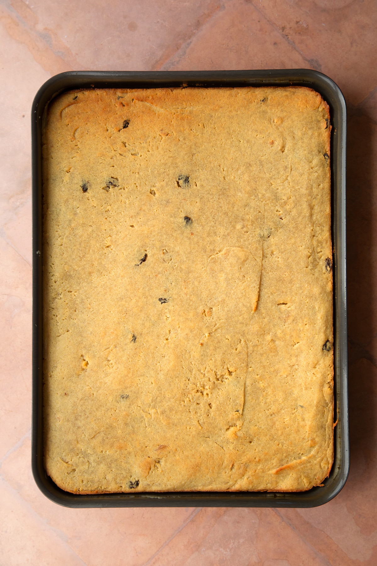 A greased tray filled with freshly baked golden semolina cake.