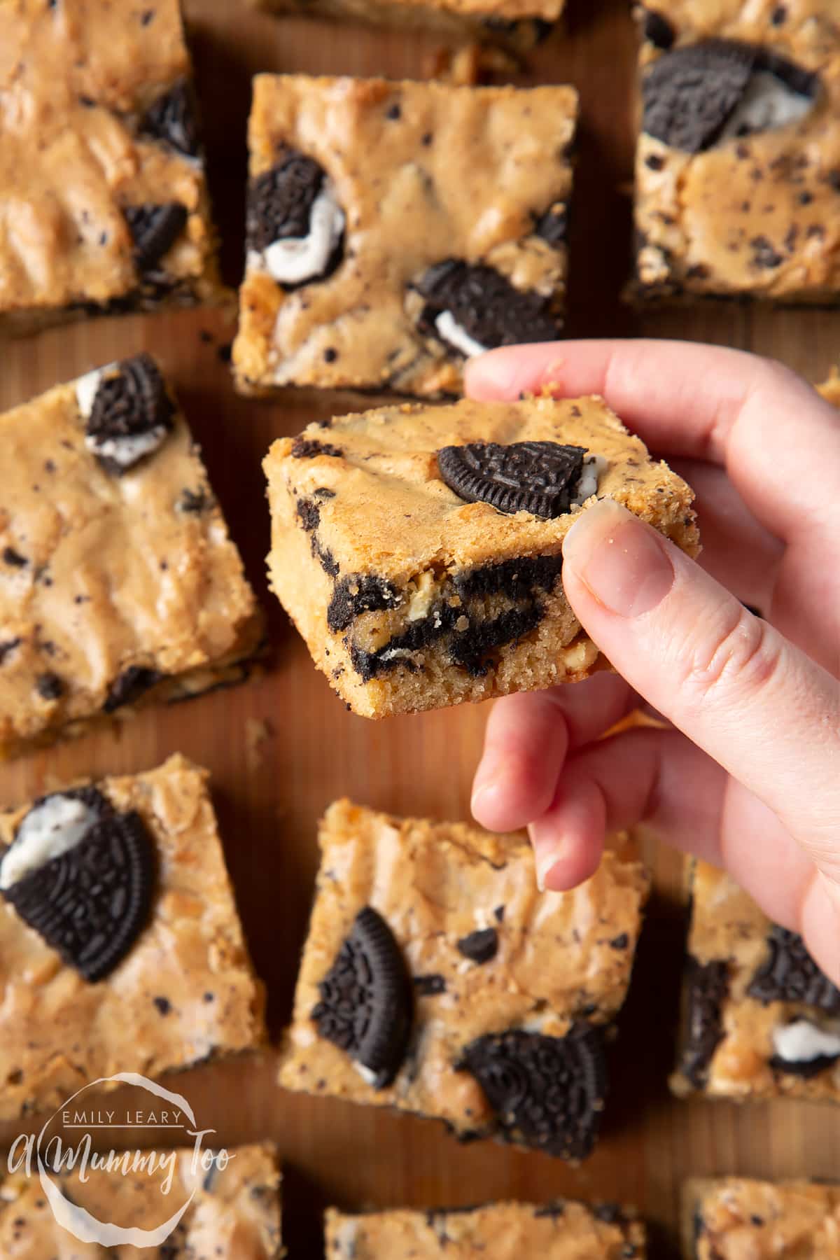 Overhead shot of a hand holding a square Oreo Blondie over a wooden board