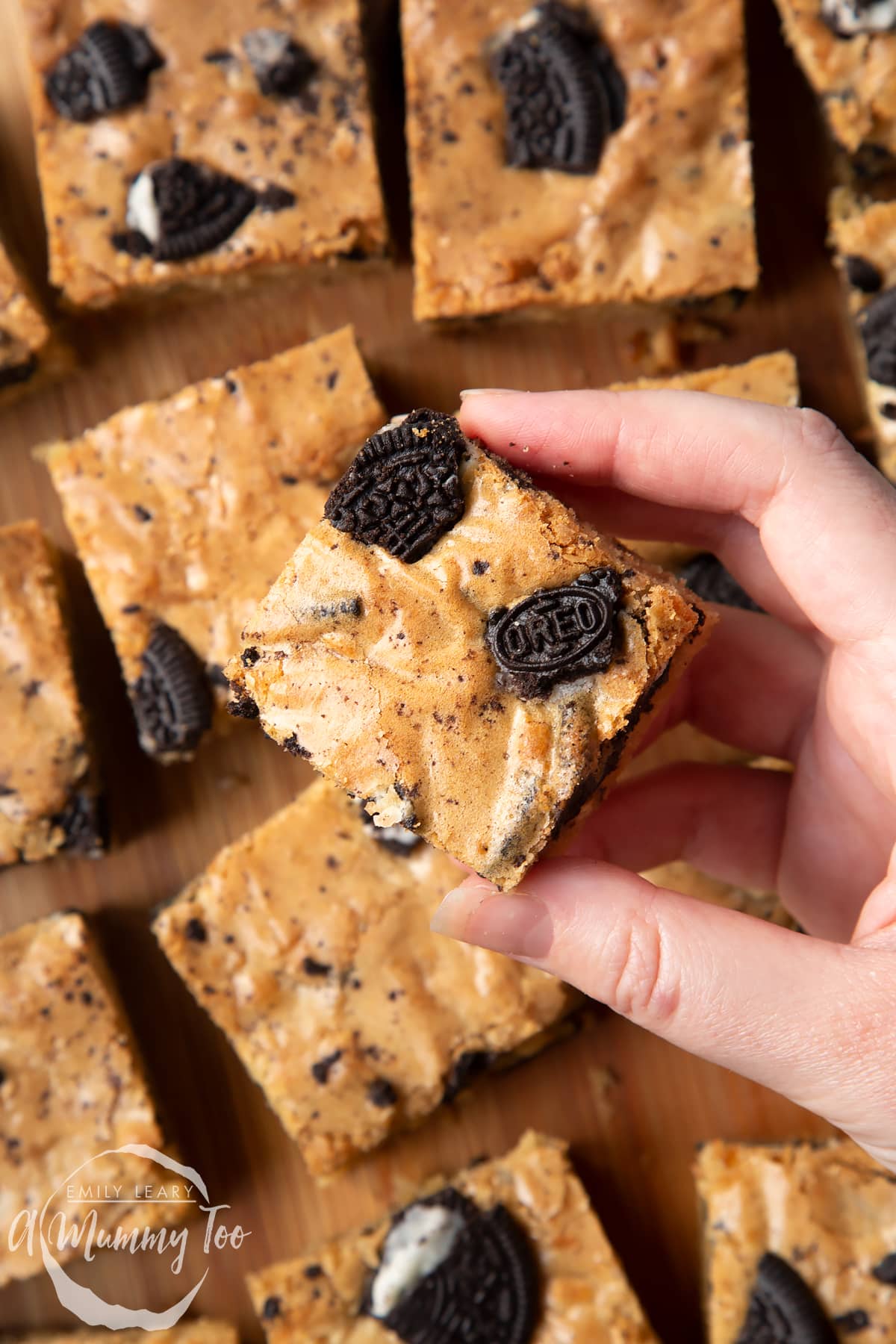 Overhead shot of a hand holding a square Oreo Blondie over a wooden board