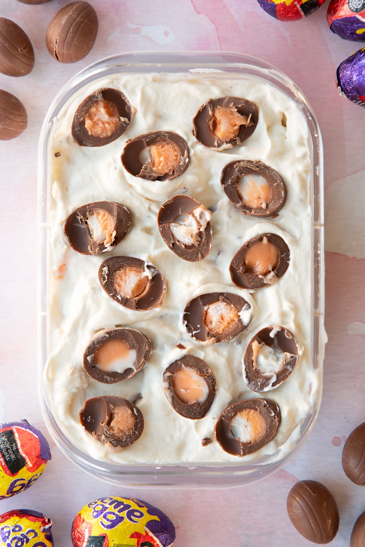 Creme Egg ice cream topped with halved Creme Egg minis and ready to freeze in oblong plastic container.