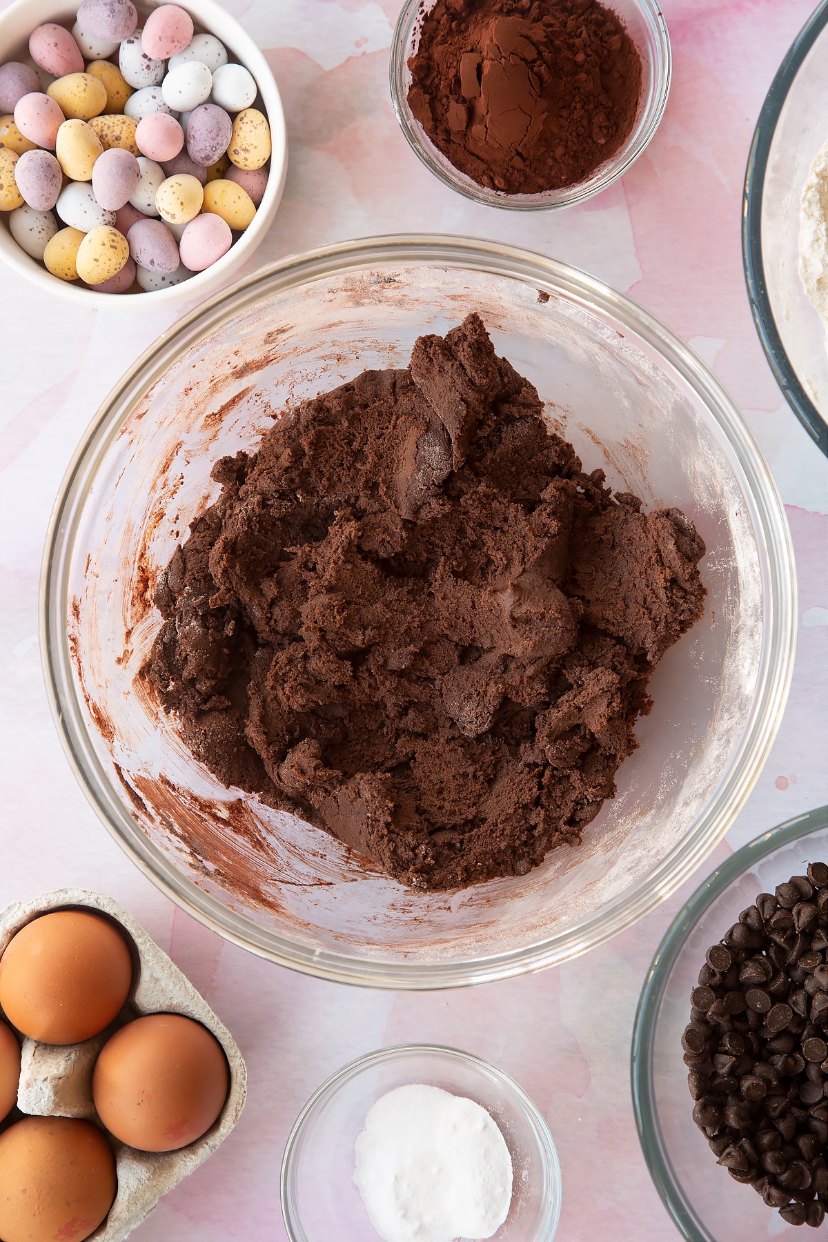 Chocolate cookie dough in a bowl. Ingredients to make Chocolate Easter cookies surround the bowl.