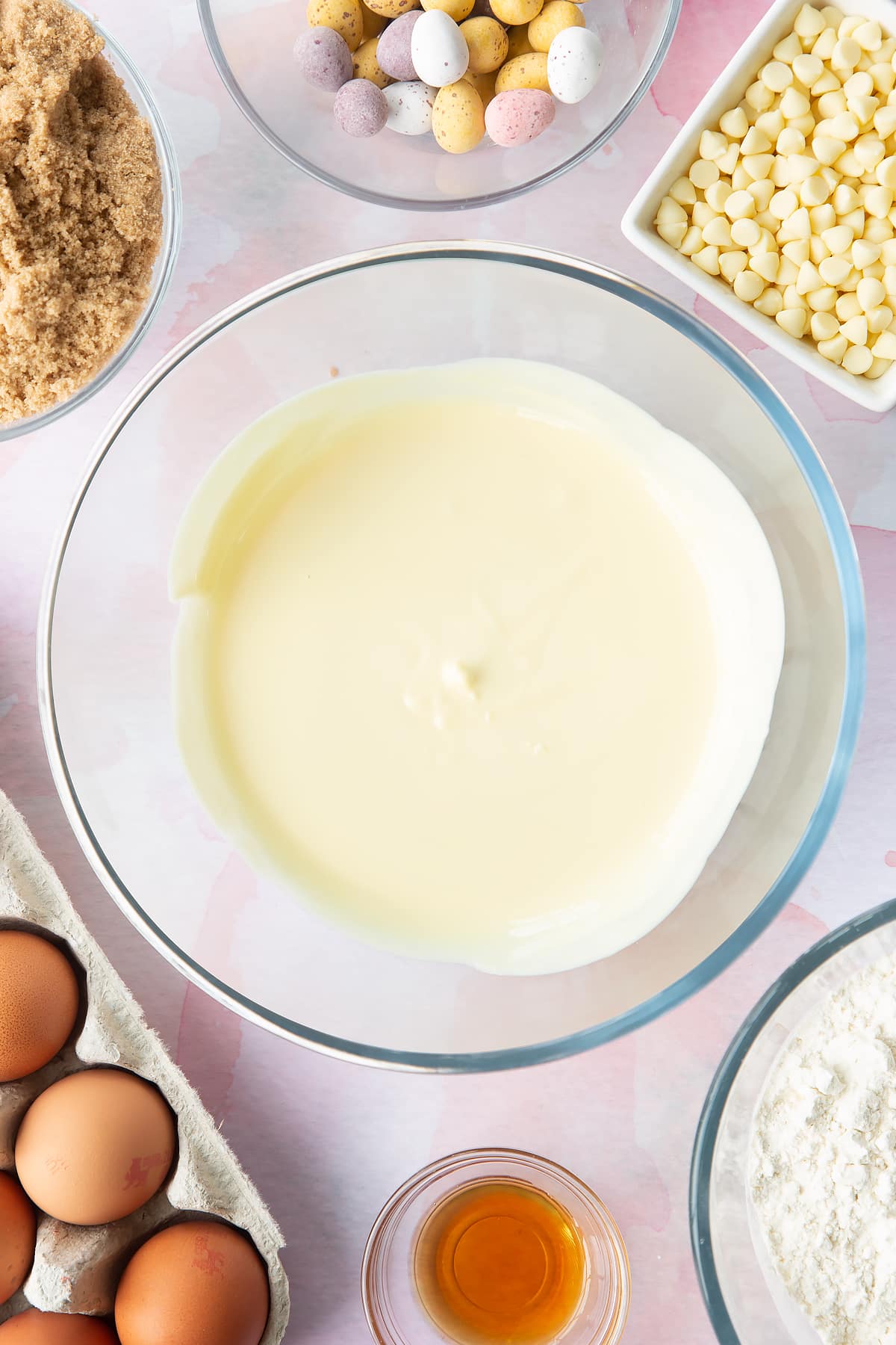 Melted white chocolate chunks in a bowl. Ingredients to make Mini Egg blondies surround the bowl.