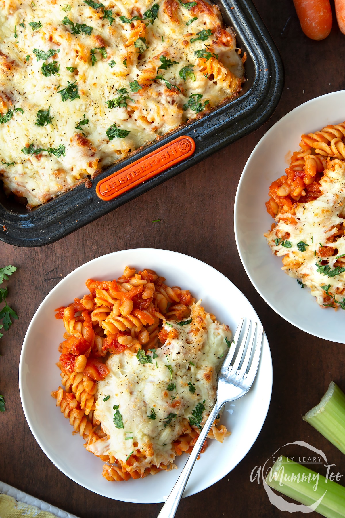 Pasta and baked beans served to white bowls with melted mozzarella. A fork rests in a bowl.