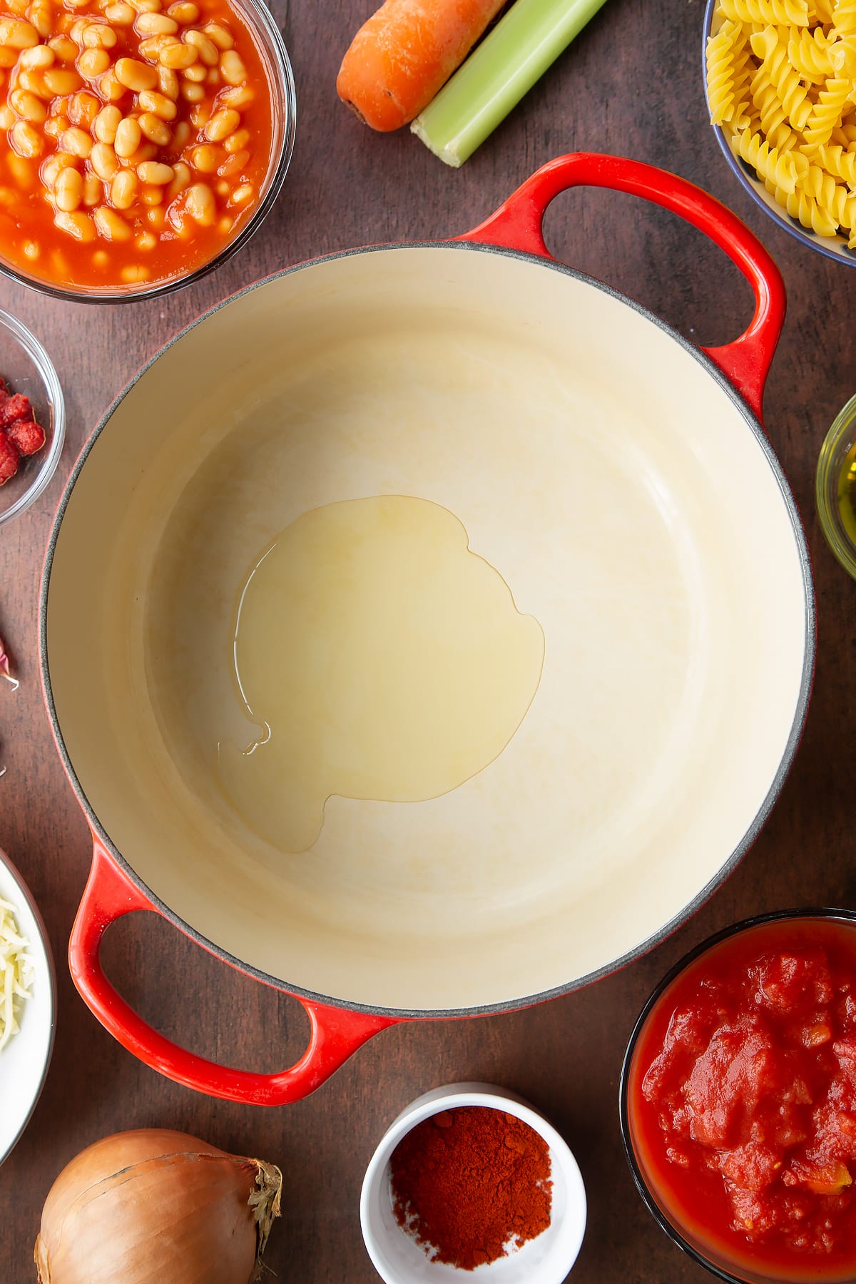 Olive oil in a saucepan. Ingredients to make pasta and baked beans surround the pan.
