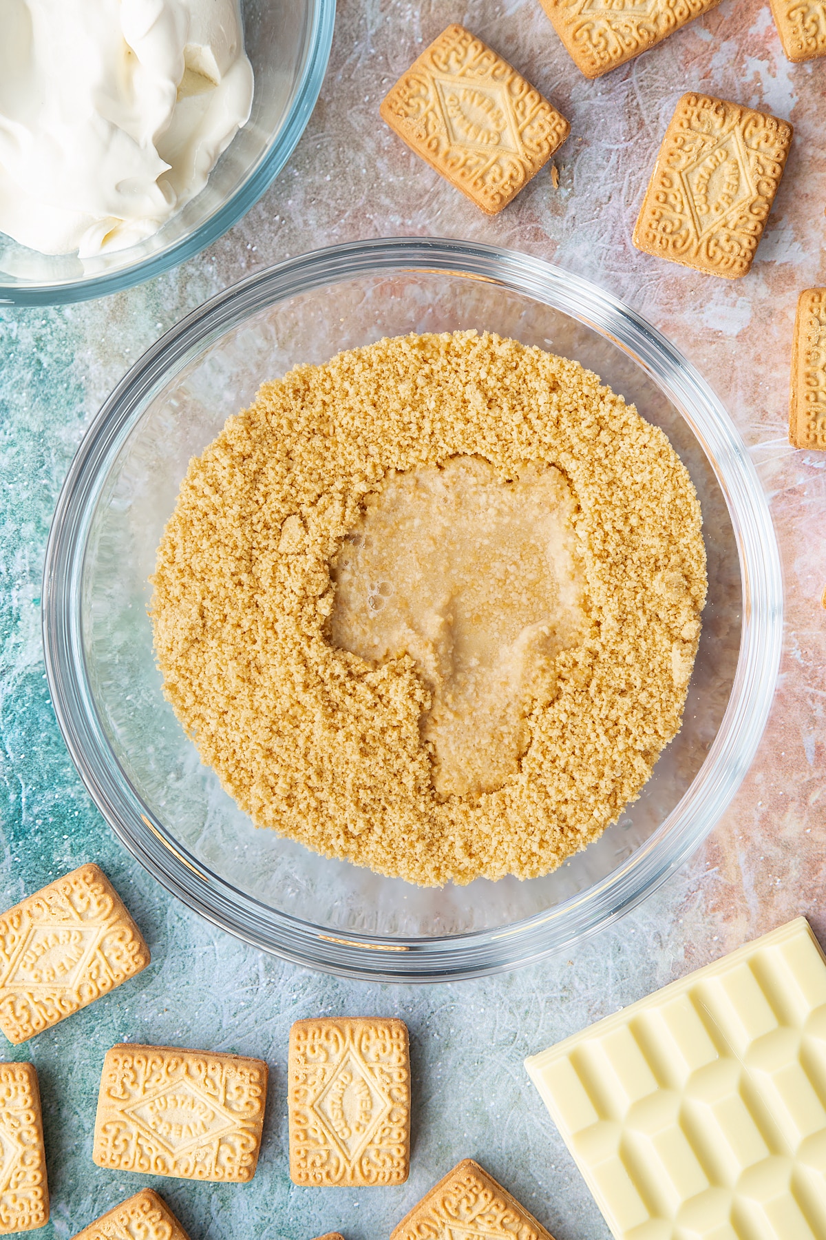 Overhead shot of biscuit crumbs and water in a large clear bowl