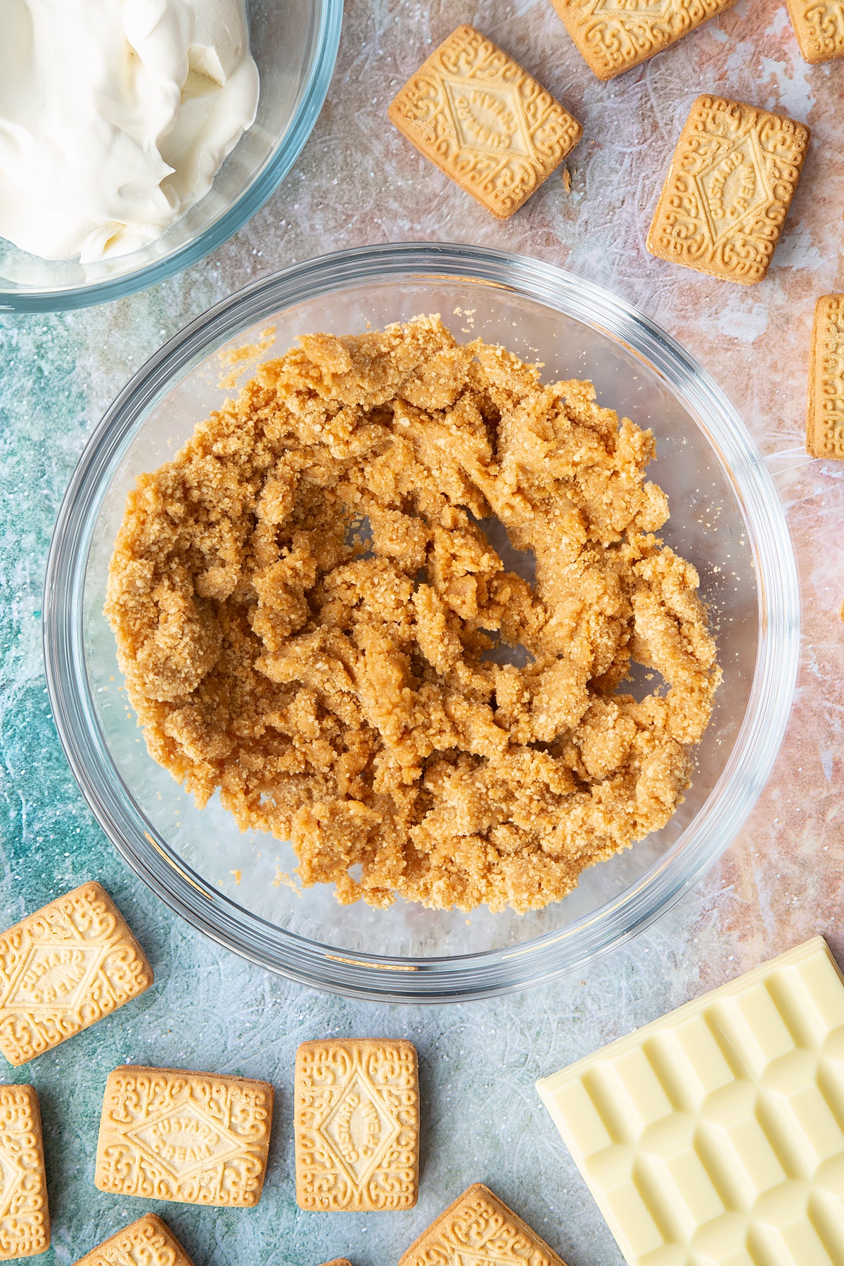 Overhead shot of custard cream biscuit crumbs mixed with water to create a dough mixture in a large clear bowl