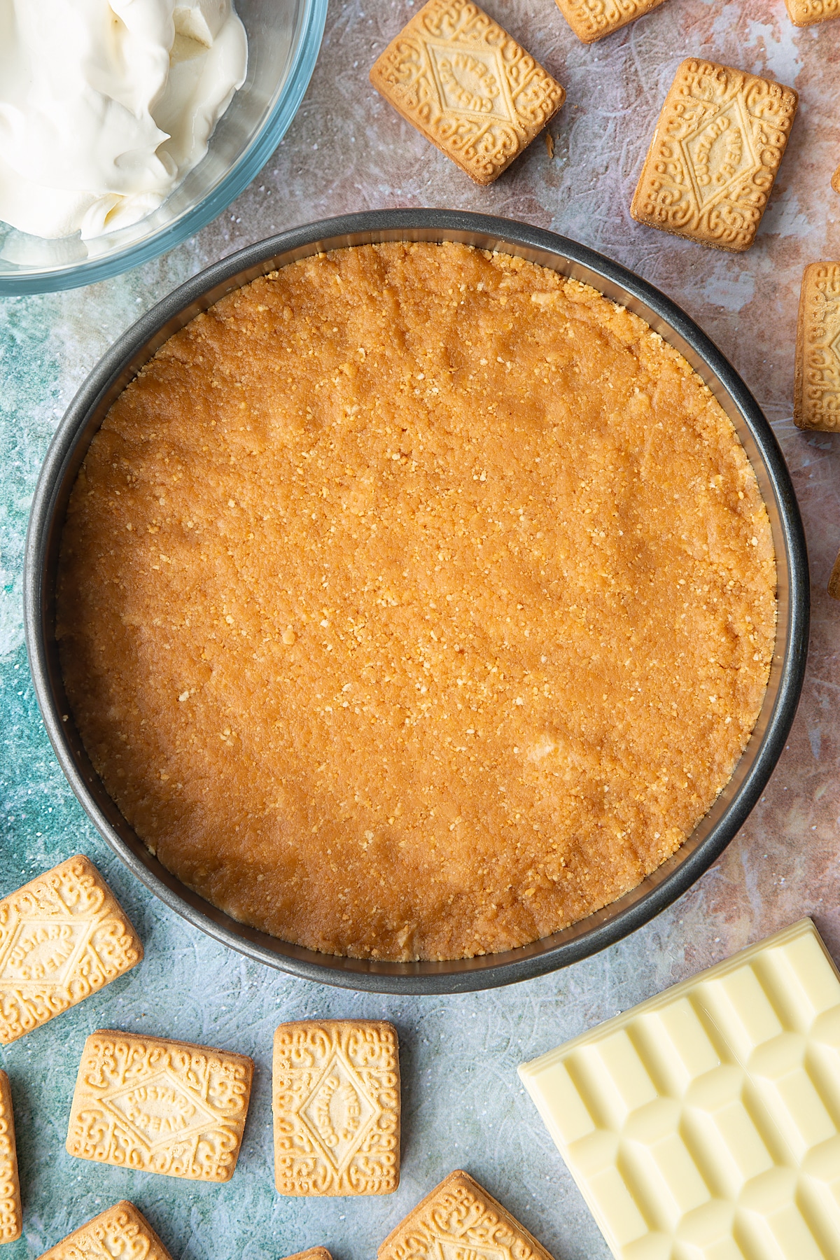 Overhead shot of custard cream biscuit crumb pressed flat into a large metal cake tin