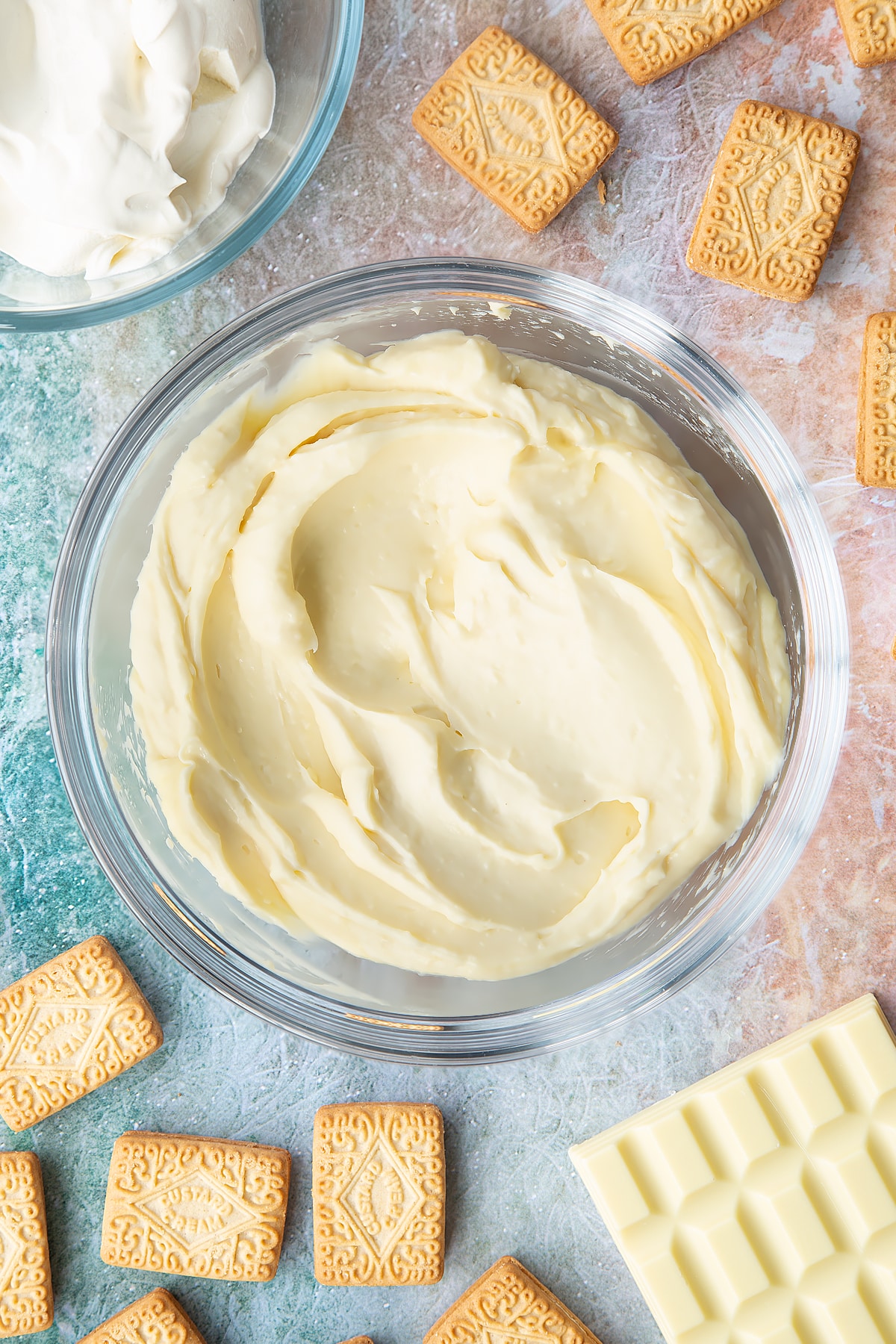 Overhead shot of melted white chocolate and cream cheese combined in a large clear bowl