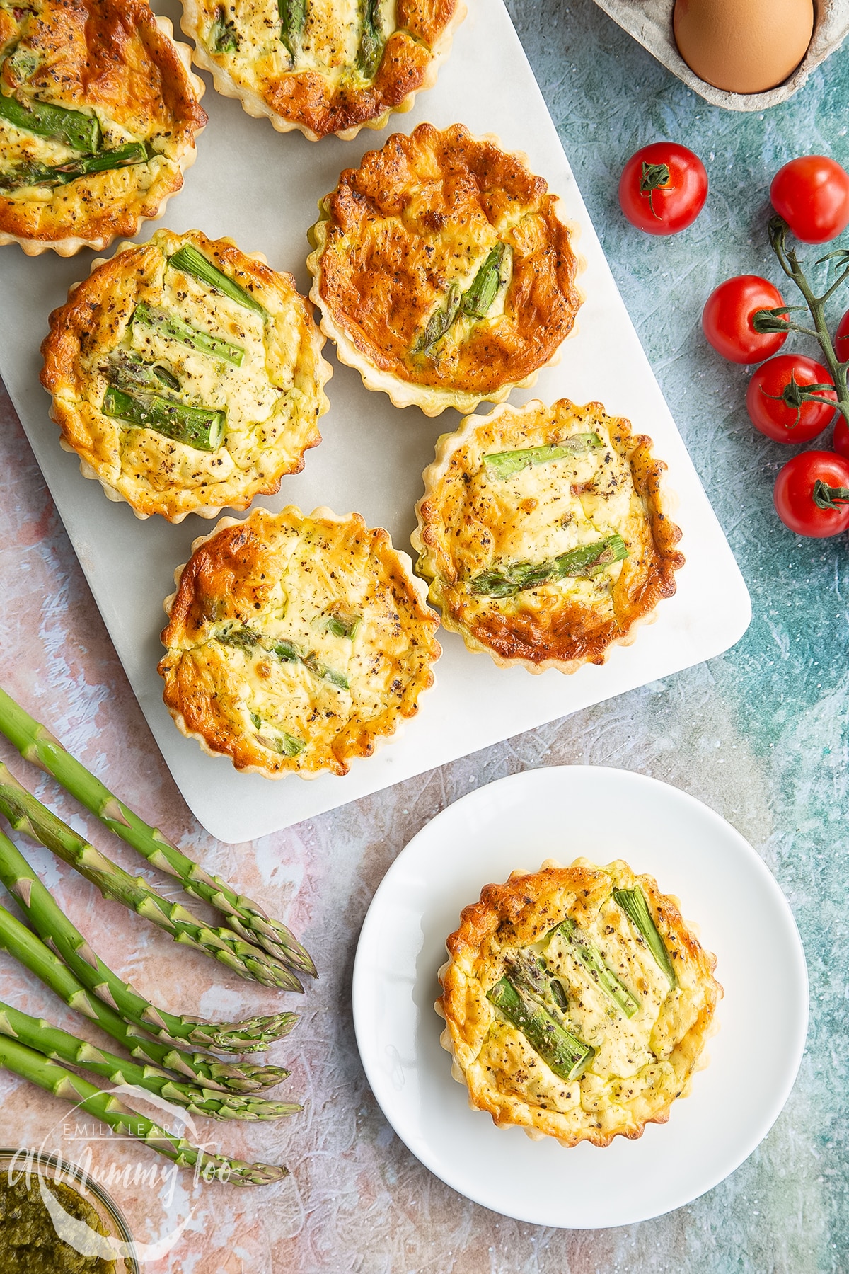 Asparagus tartlets on a white marble board. One is on a white plate. Shown from above.