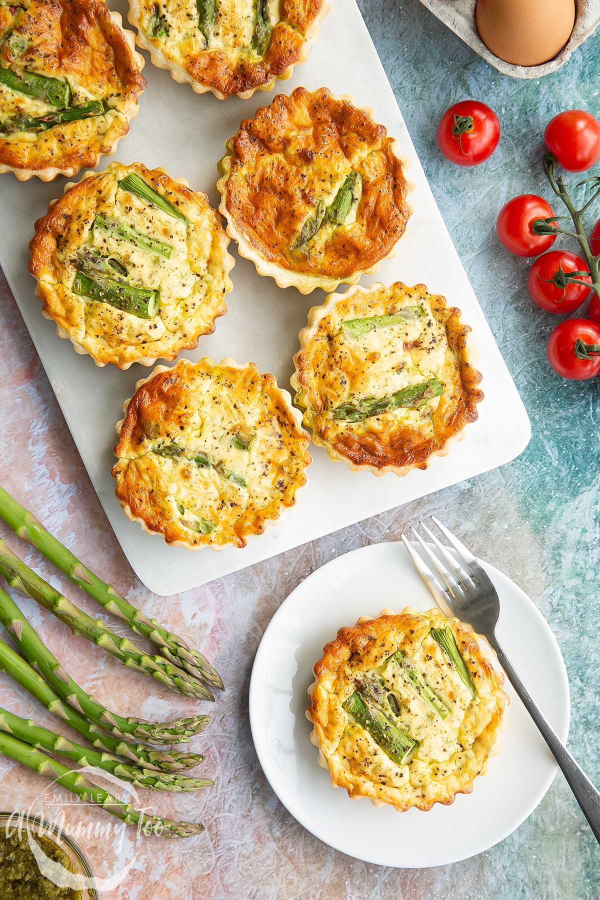 Asparagus tartlets on a white marble board. One is on a white plate with a fork. Shown from above.