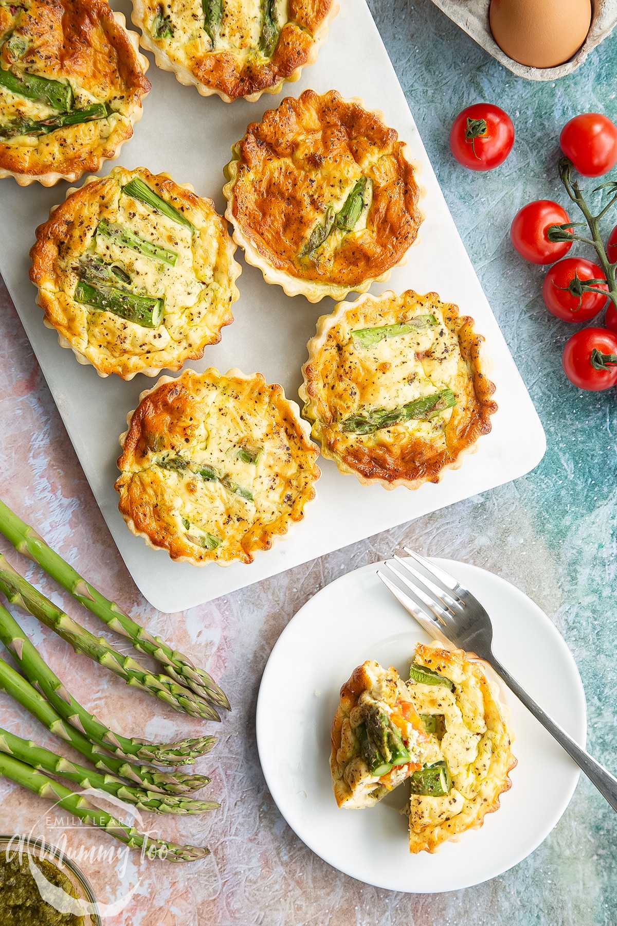 Asparagus tartlets on a white marble board. One is on a white plate with a fork. It has been cut up. Shown from above.