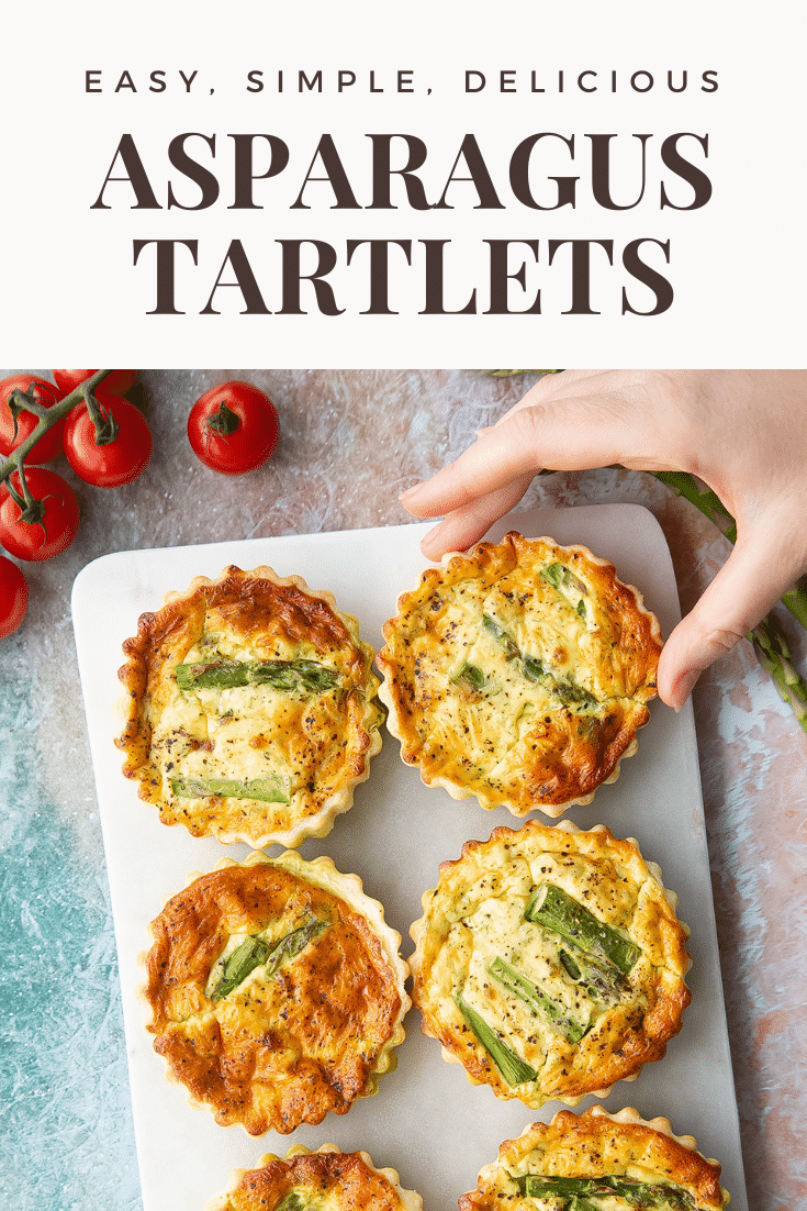 Asparagus tartlets on a white marble board. A hand reaches for one. Caption reads: easy, simple, delicious asparagus tartlets