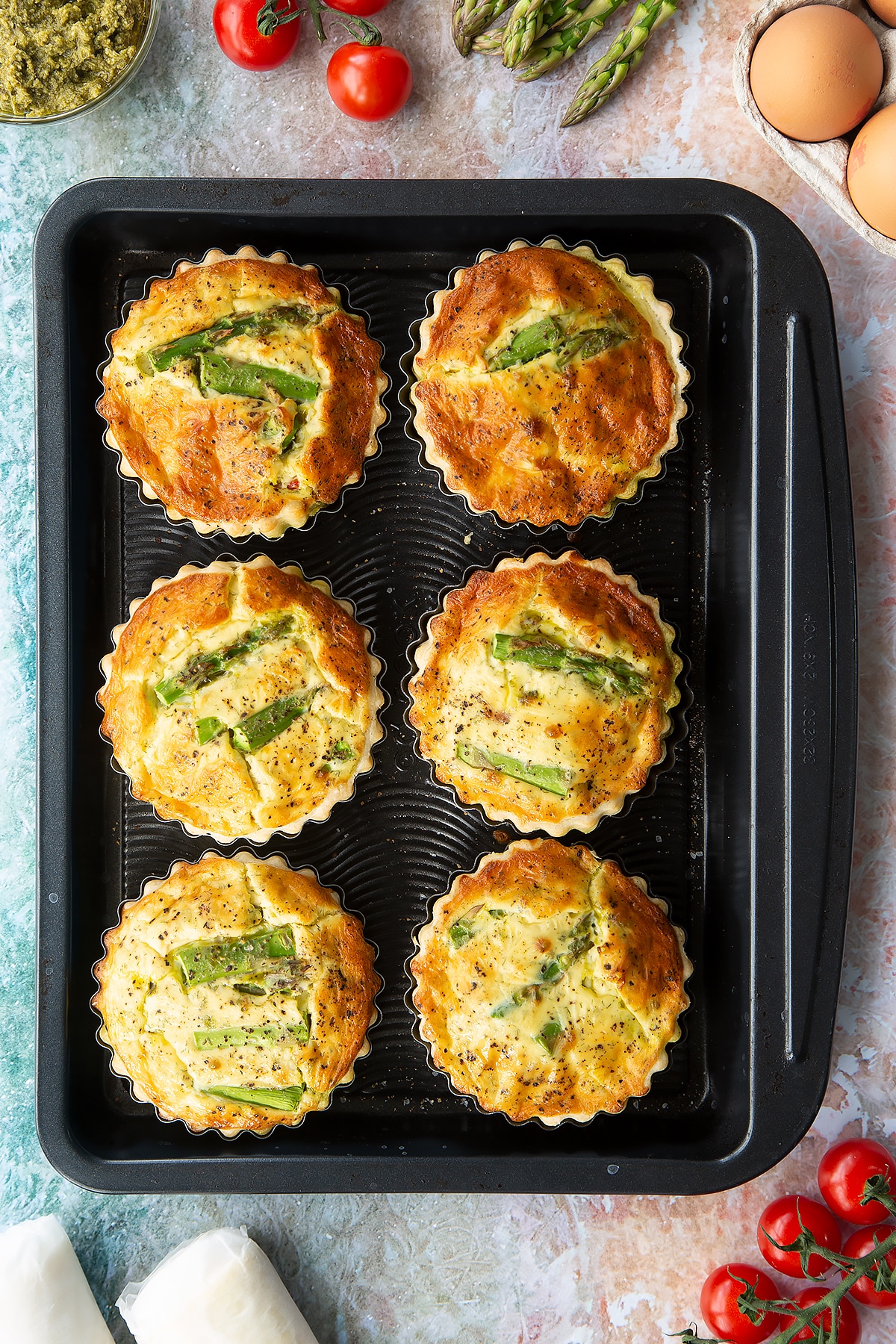 Six asparagus tartlets on a baking tray. Shown from above.