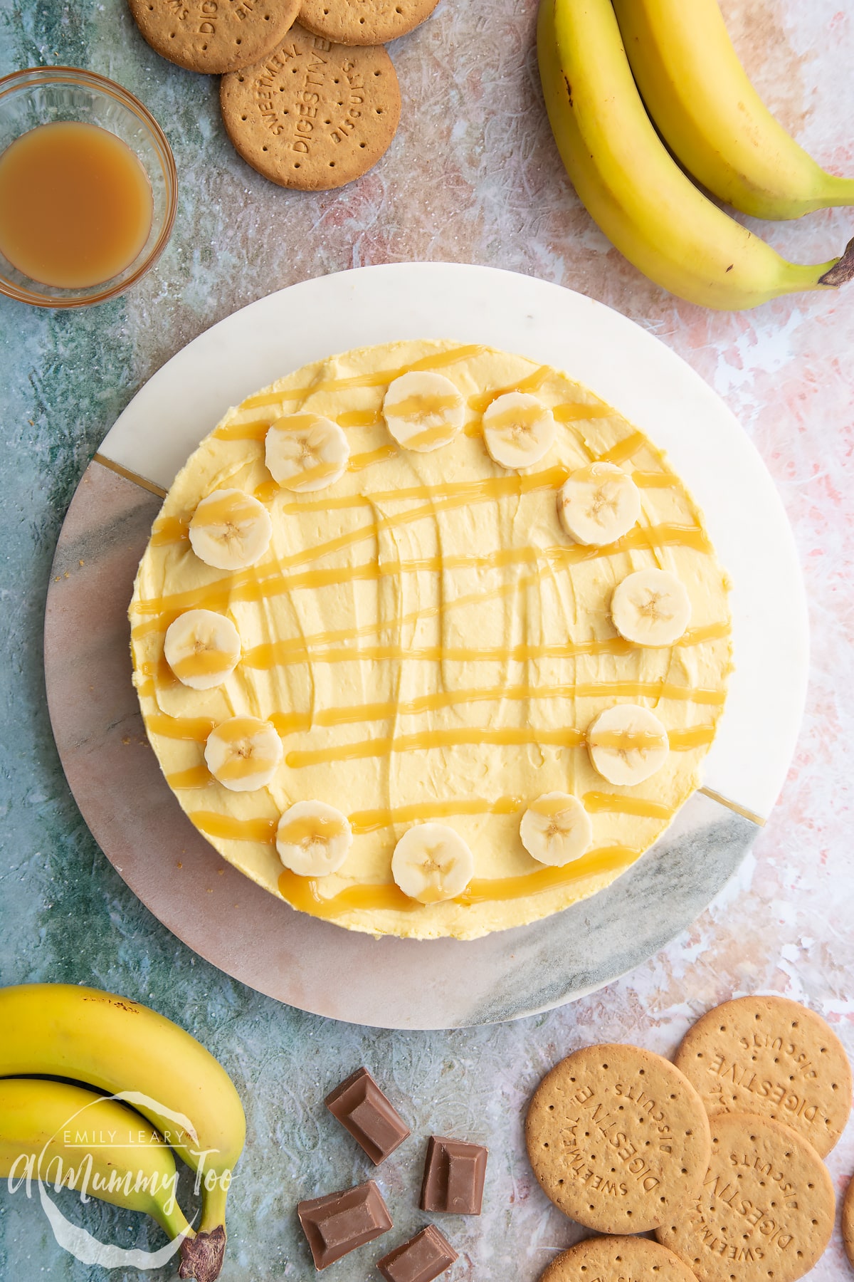 Banoffee pie cheesecake topped with banana slices and drizzled with toffee sauce on a white and pink marble board.