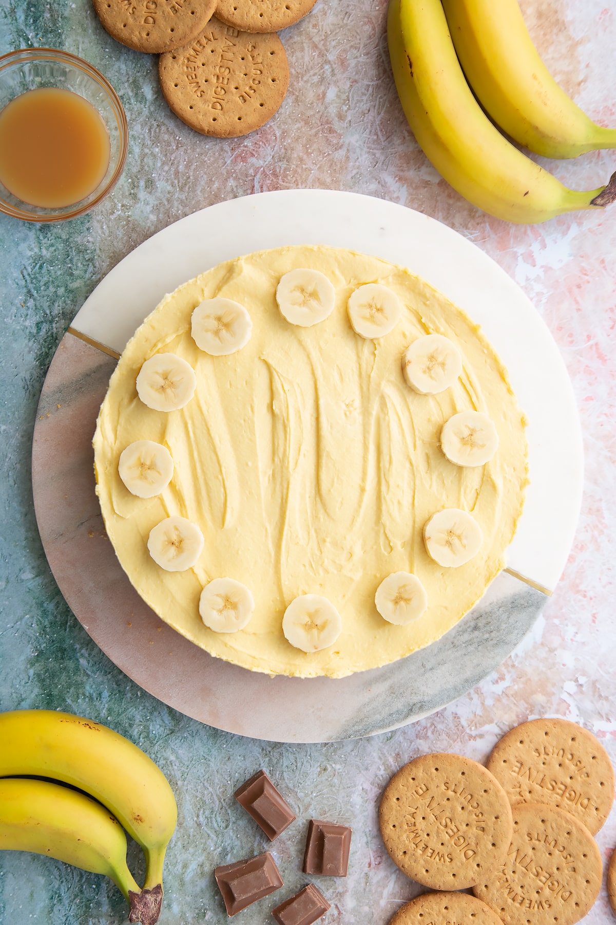 Banoffee pie cheesecake topped with banana slices on a white and pink marble board.