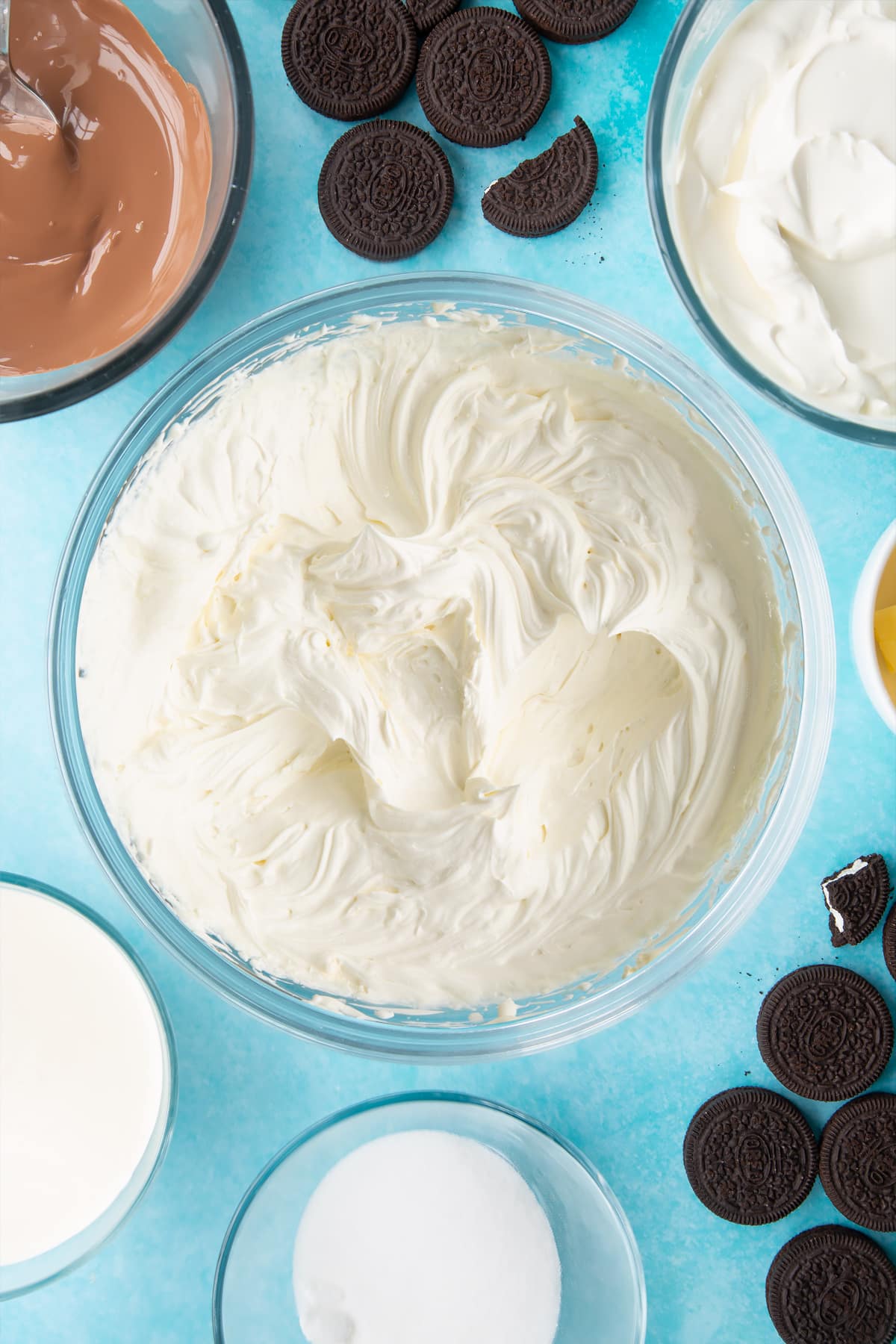 Overhead shot of whipped cream, cream, sugar and cream cheese mixed together in a large clear bowl