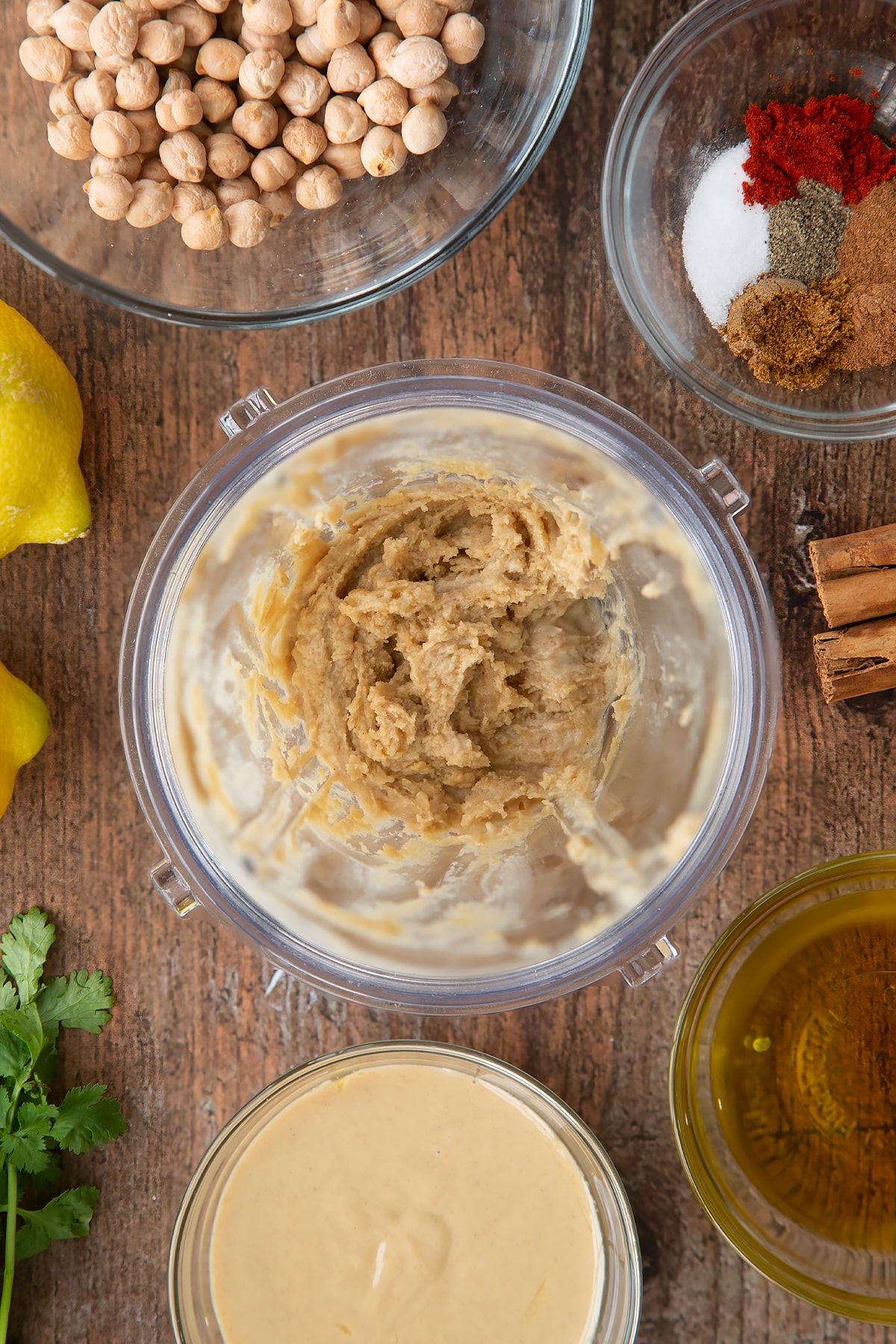 Tahini and lemon juice whipped in a small blender bowl. Ingredients to make cinnamon hummus surround the bowl.
