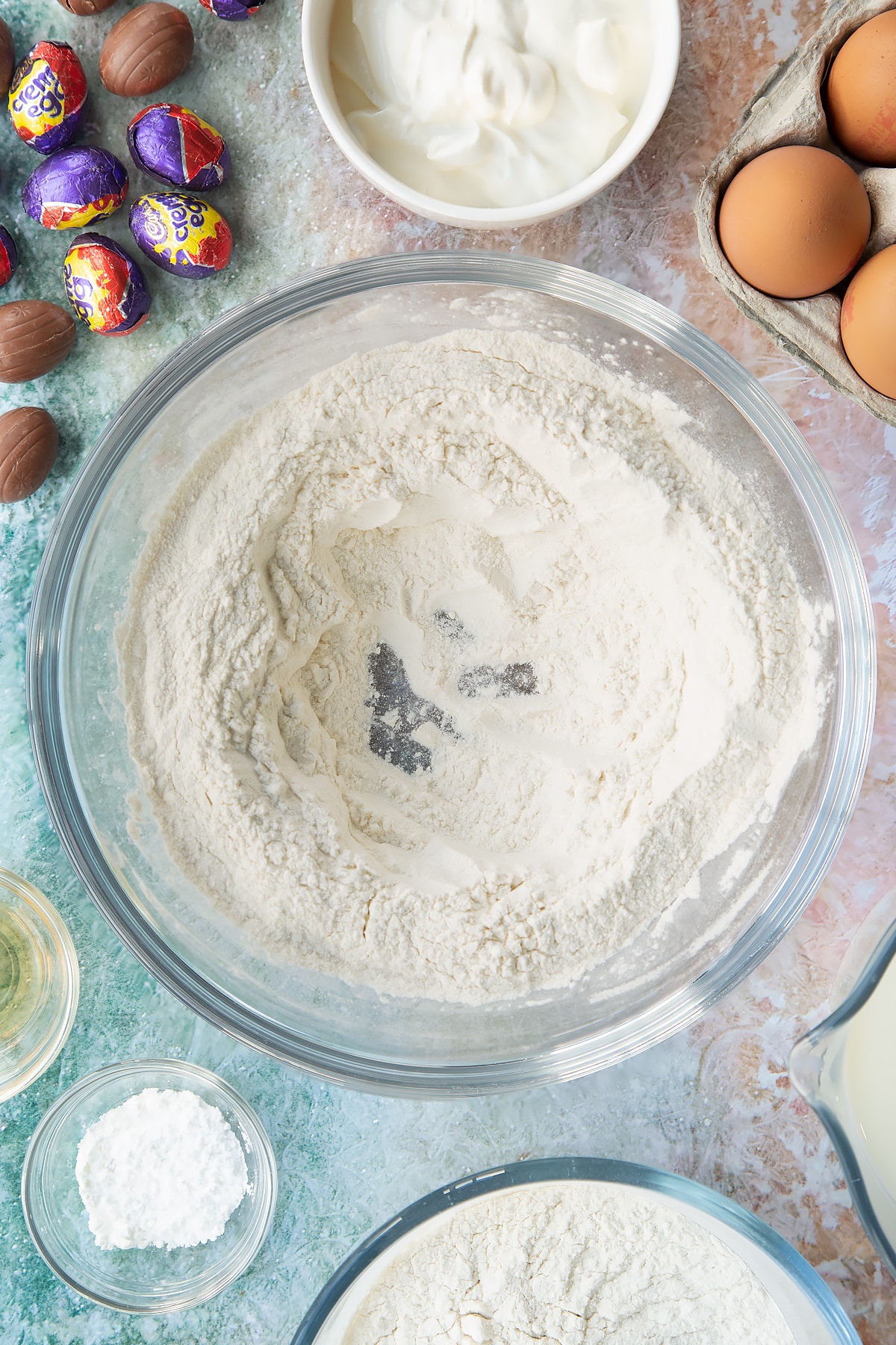 Self-raising flour and baking powder in a bowl with a well in the centre. Ingredients to make Creme Egg pancakes surround the bowl.