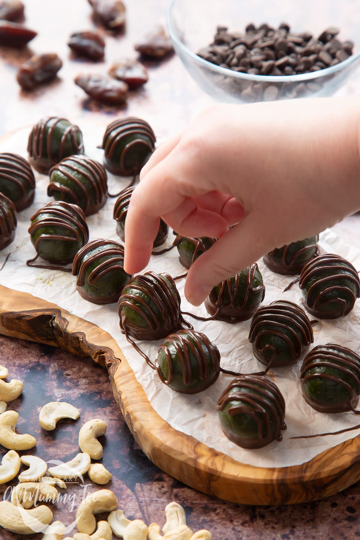 Close up of matcha protein balls on a wooden board lined with baking paper. A hand reaches for one.