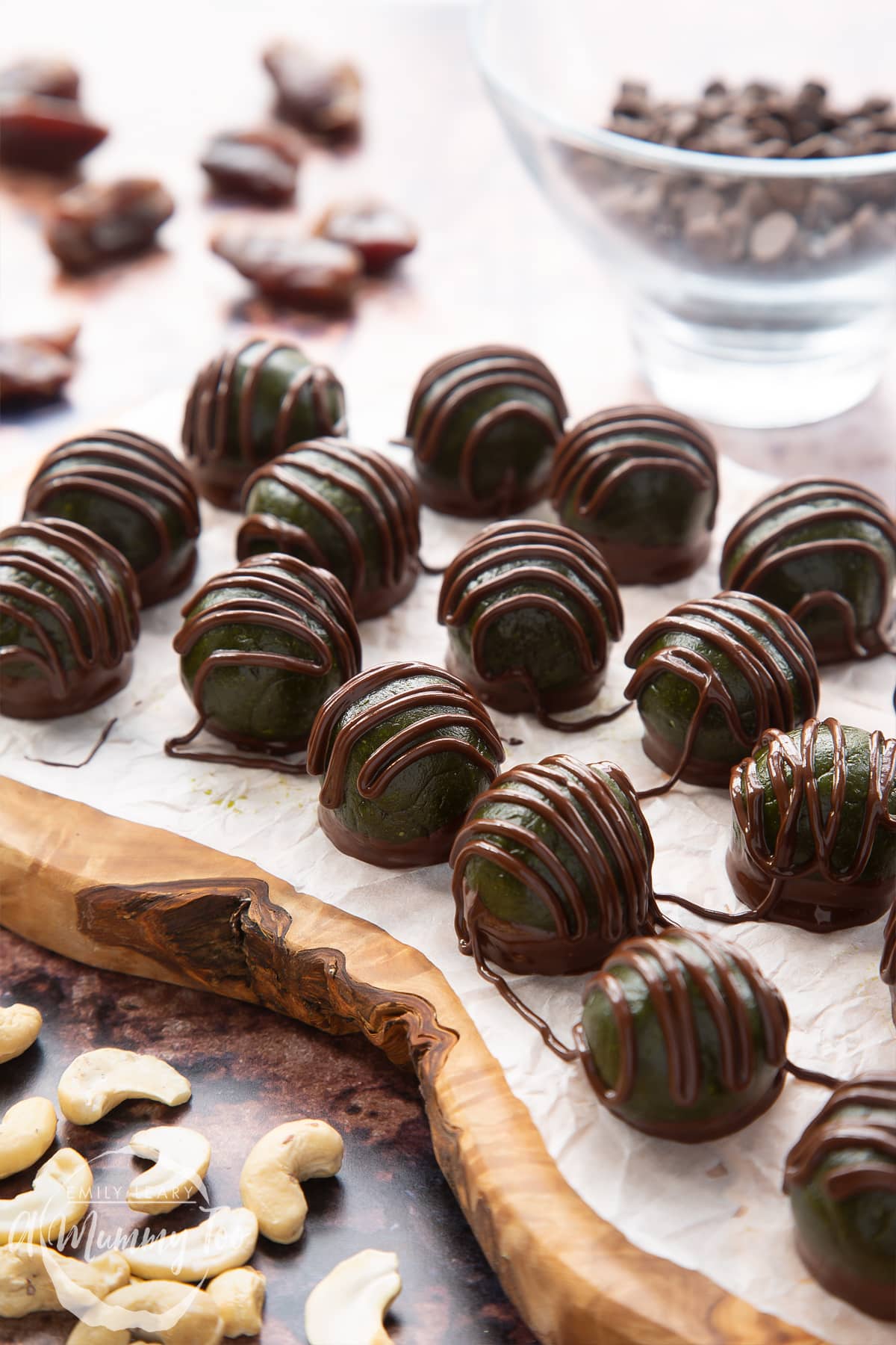 Close up of matcha protein balls on a wooden board lined with baking paper. The balls are dark green and have been drizzled with melted dark chocolate.