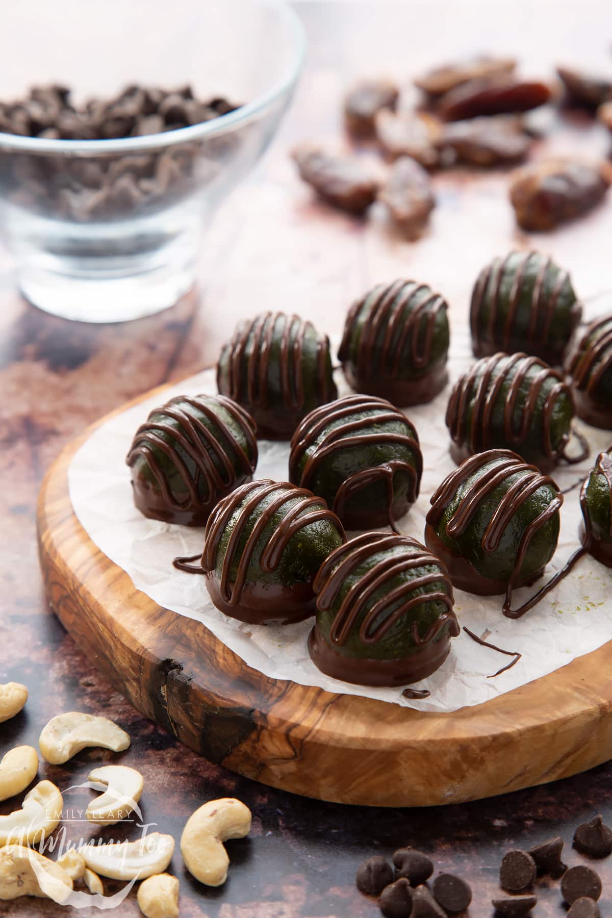 Close up of matcha protein balls on a wooden board lined with baking paper. The balls are dark green and have been drizzled with dark chocolate.