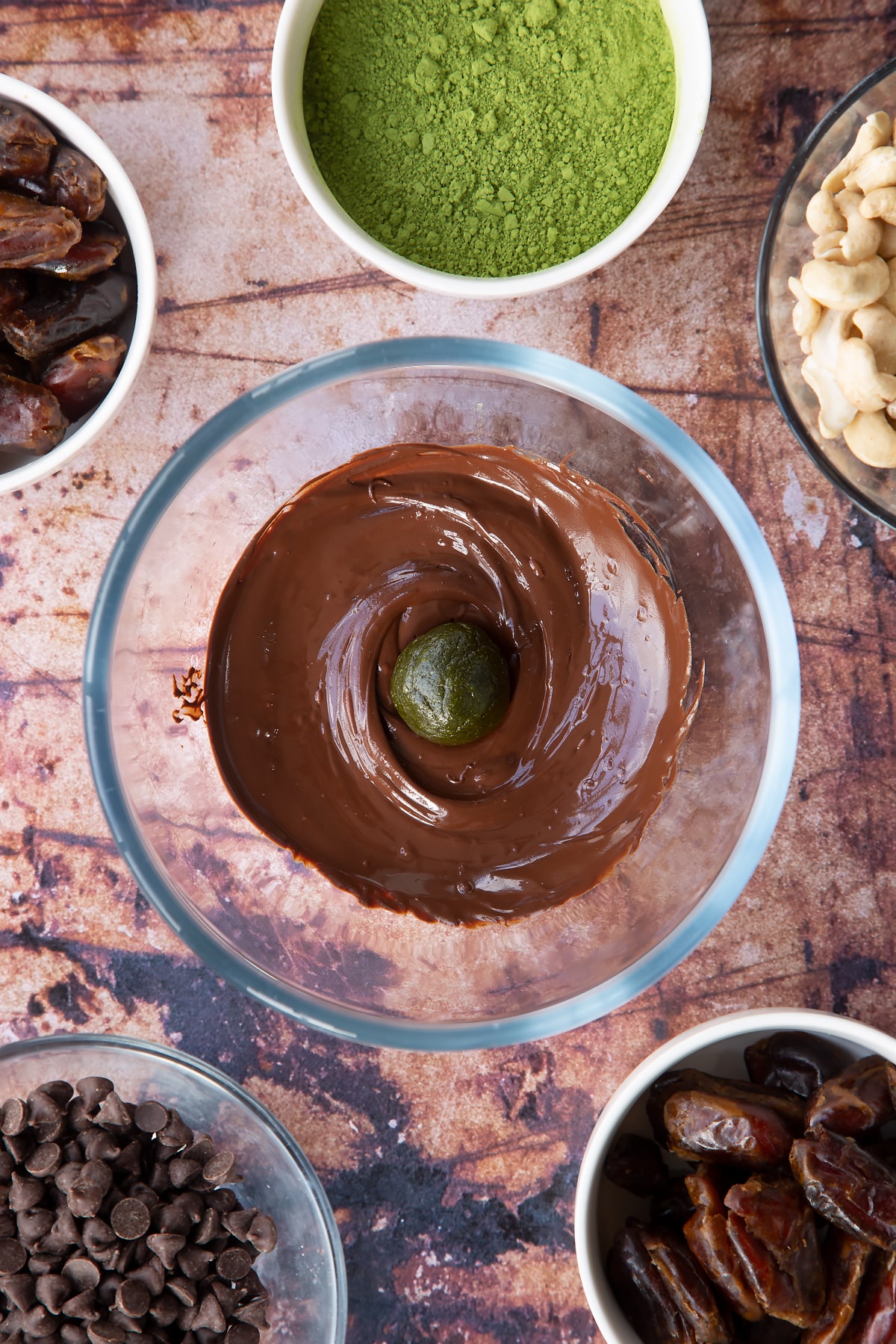 Melted dark chocolate in a mixing bowl with a matcha protein ball in the centre.
