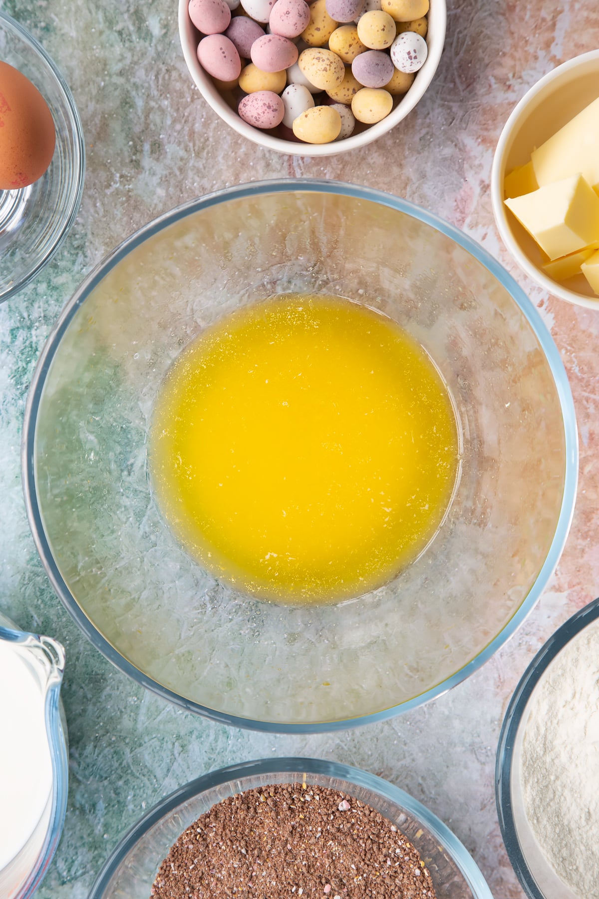 Melted butter in a bowl. Ingredients to make Mini egg waffles surround the bowl.