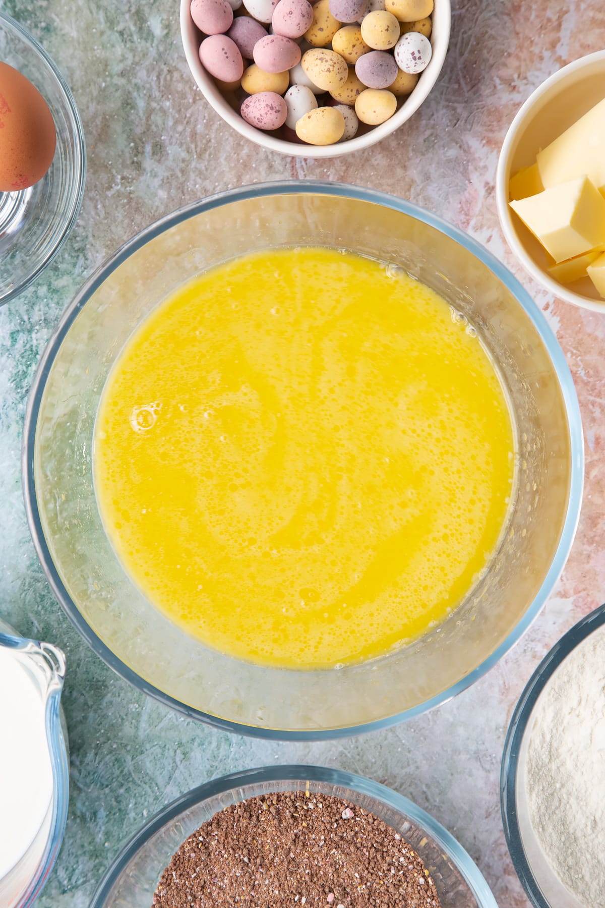 Melted butter, milk and eggs in a bowl. Ingredients to make Mini egg waffles surround the bowl.