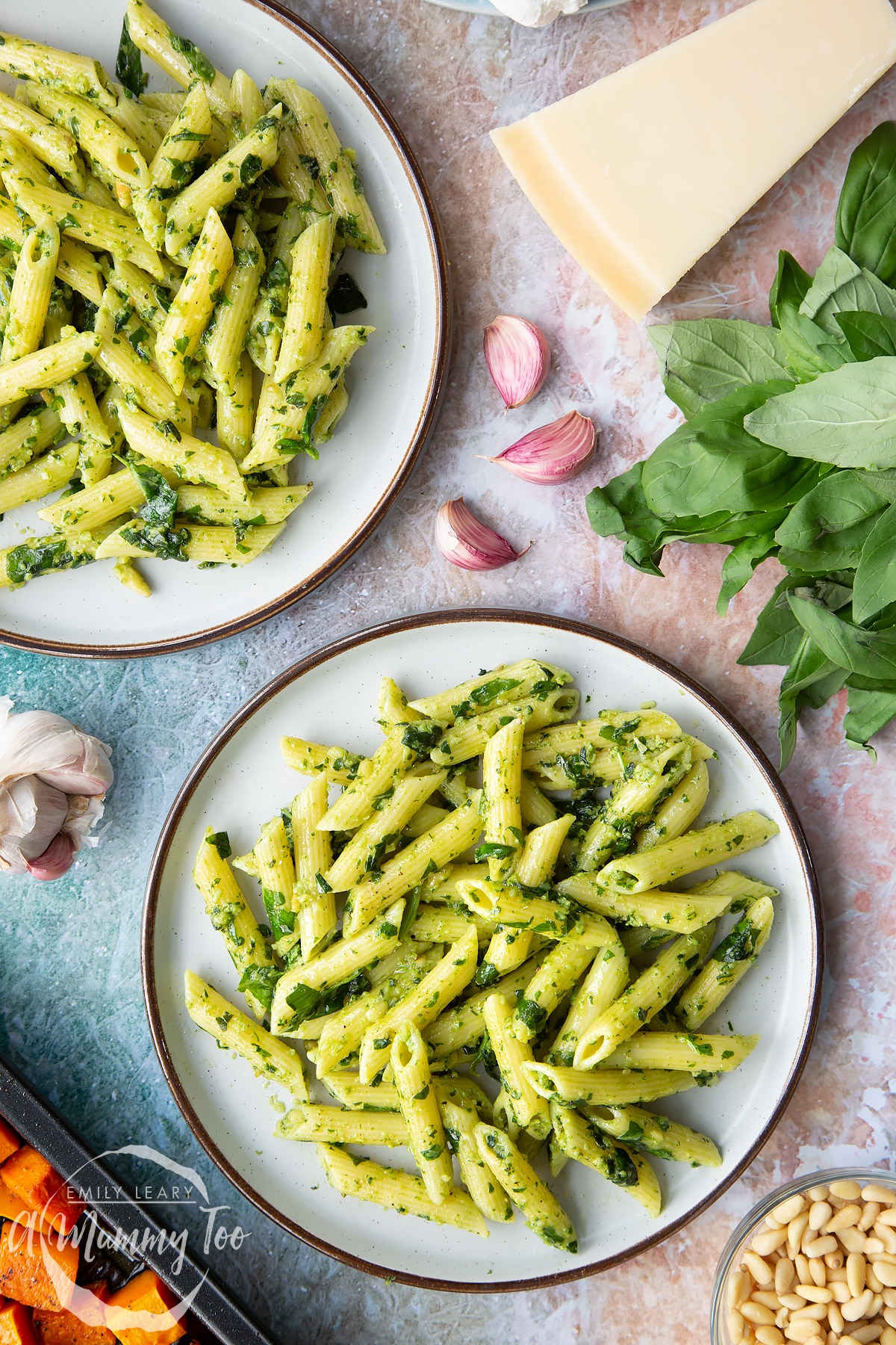 Penne pasta tossed with fresh pesto served to plates. Ingredients to make penne with butternut squash and goat cheese surround the plates.