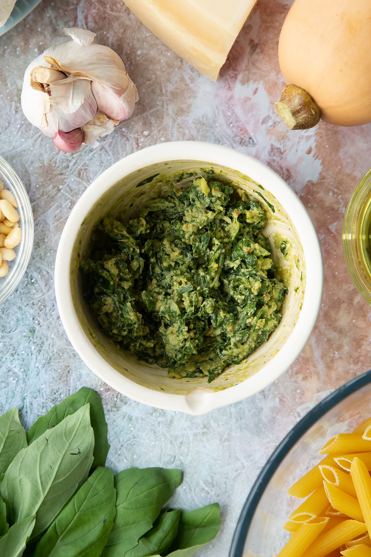 Toasted pine nuts, garlic, pepper and basil crushed in a small mortar. Ingredients to make penne with butternut squash and goat cheese surround the mortar.